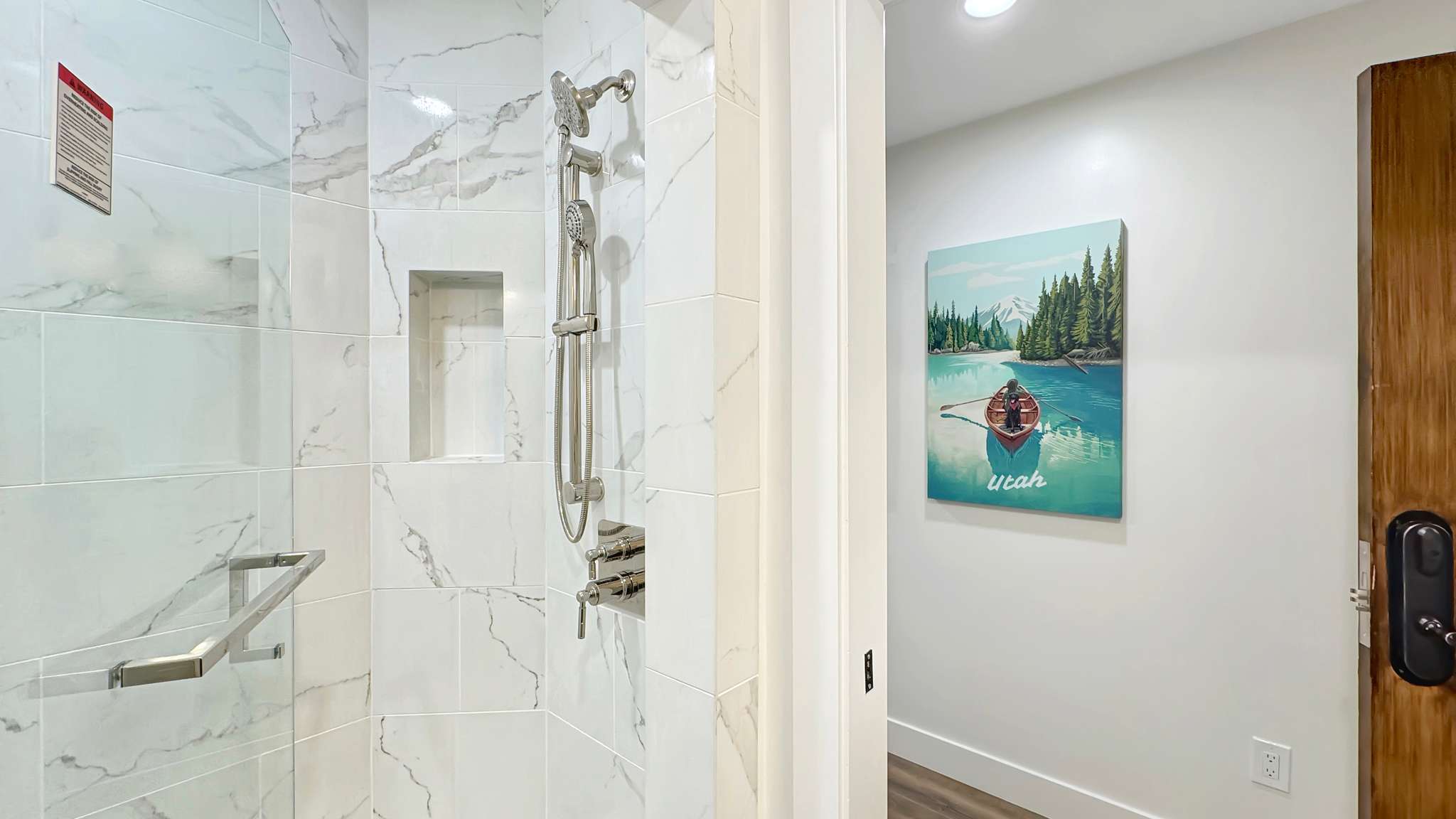 Shower featuring white marble-look tile, brushed nickel fixtures, a built-in shower niche, and a grab bar