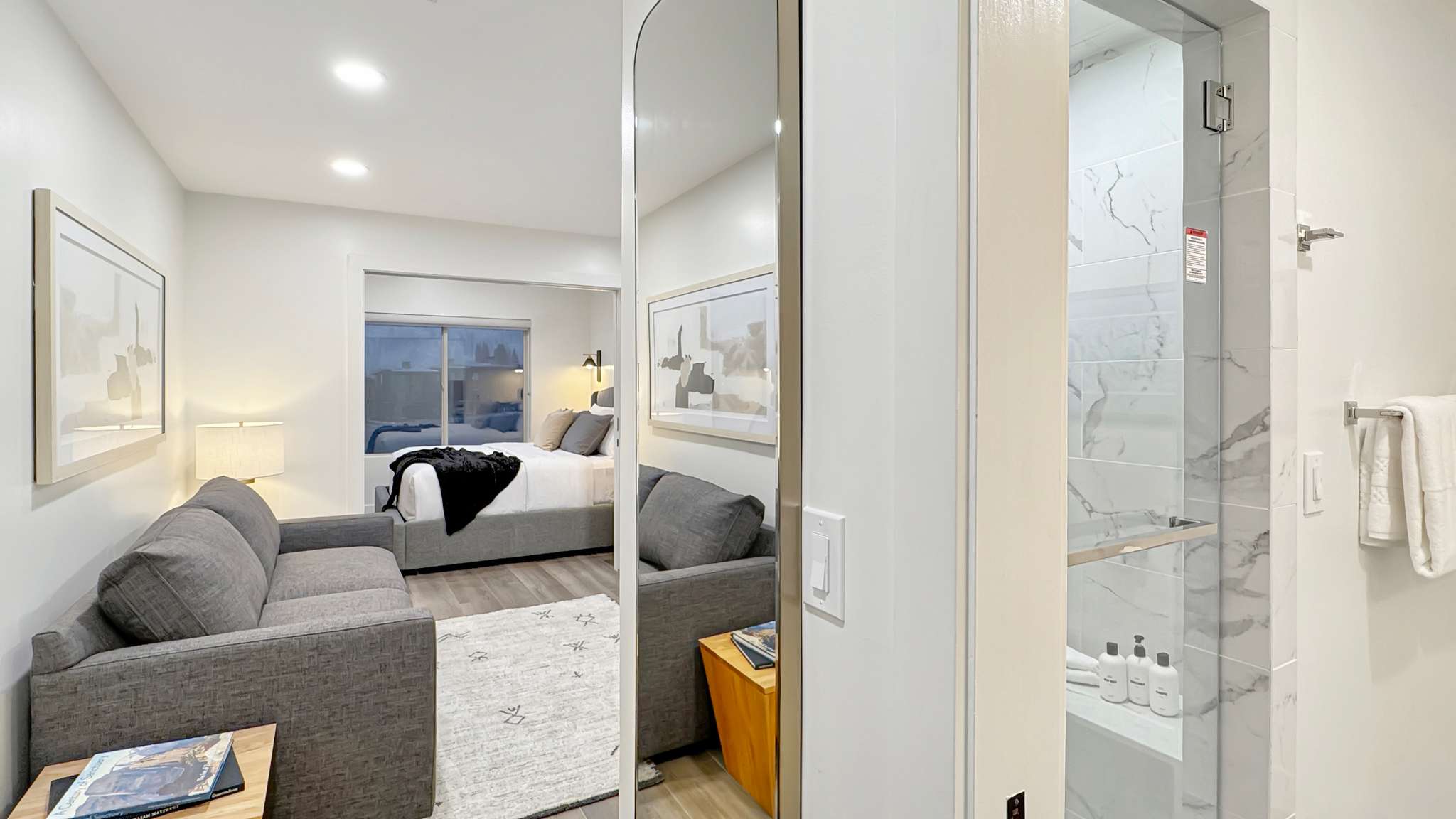 Open-concept living space with recessed lighting, wood-finish flooring, and a glass-enclosed shower featuring large format marbled tile