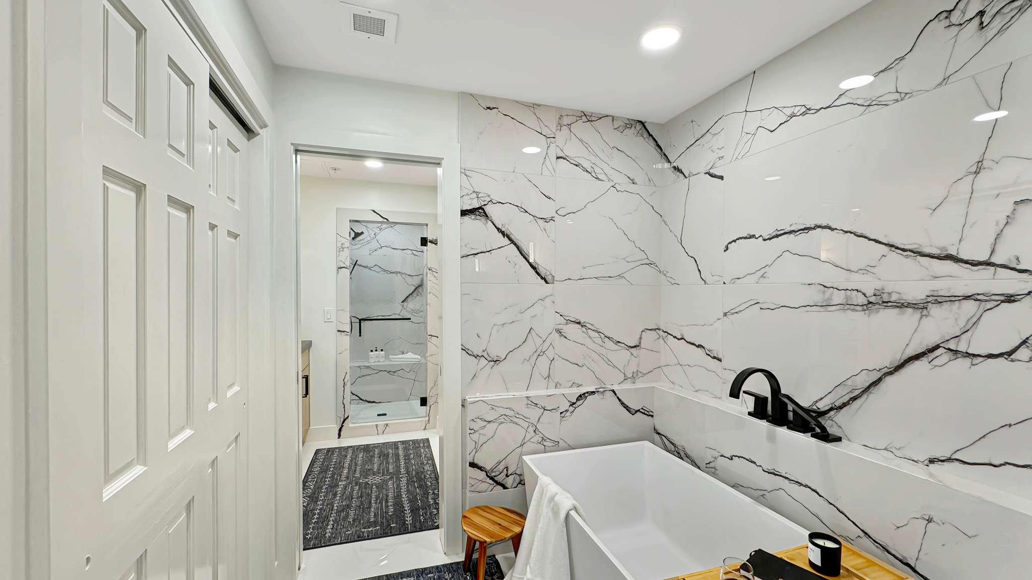 White tiled accent wall featuring black veining, freestanding soaking tub with matte black fixtures, and a glass-enclosed shower