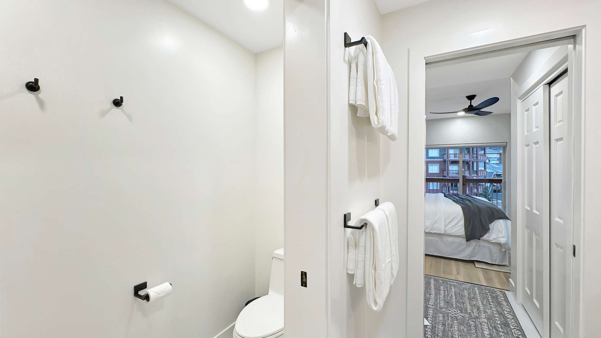Recessed lighting illuminates a bathroom featuring a toilet with a white tank and bowl, and matte black hardware including towel bars, wall hooks, and a toilet paper holder