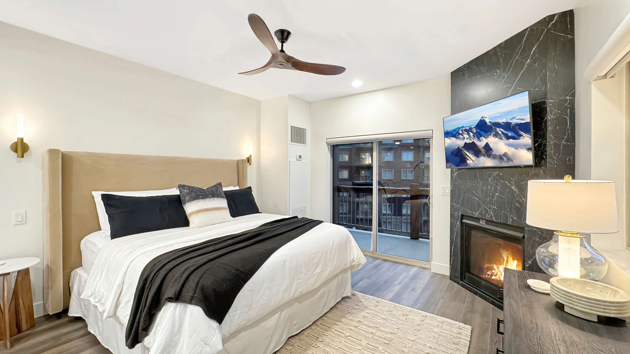 Bedroom featuring wood-finish flooring, a wall-mounted fireplace with a dark stone surround, and an overhead ceiling fan