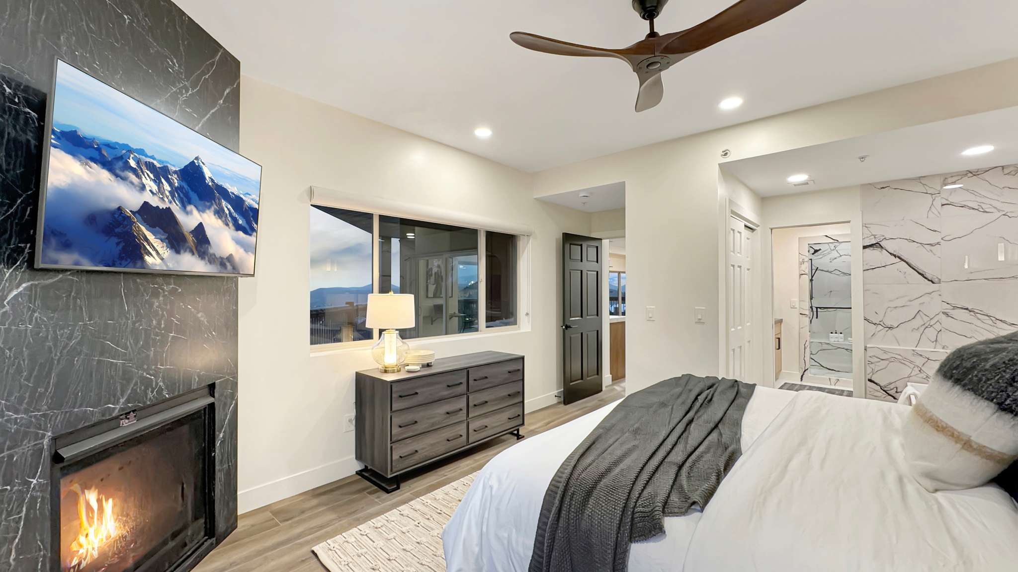 Contemporary bedroom featuring a black marble-style fireplace surround with an integrated television, wood-finish flooring, and recessed lighting