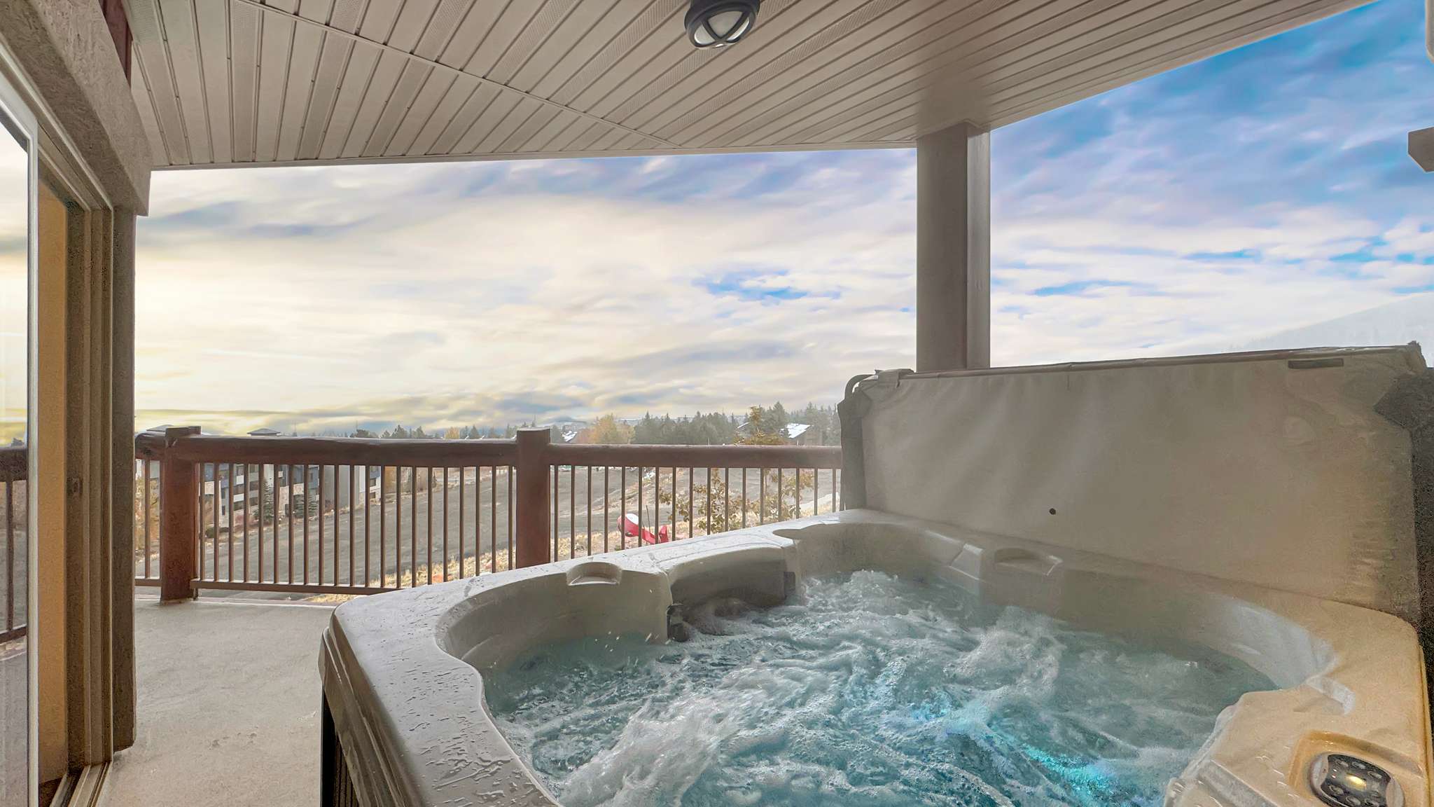 Covered deck featuring an integrated hot tub with active jets, a wood-finish railing, and sliding glass door access