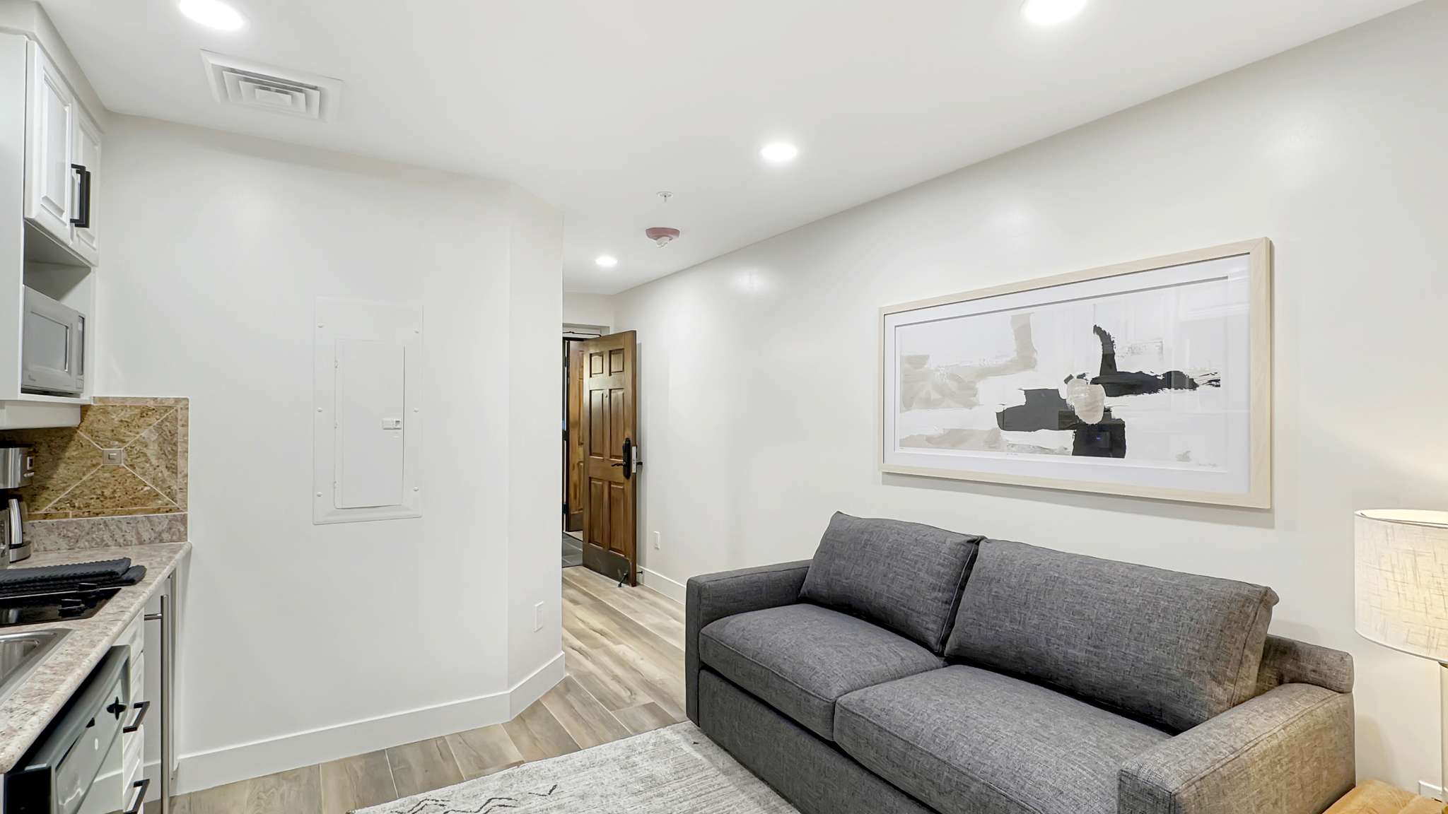 Compact living area featuring light wood-finish flooring, recessed lighting, and a partial kitchenette