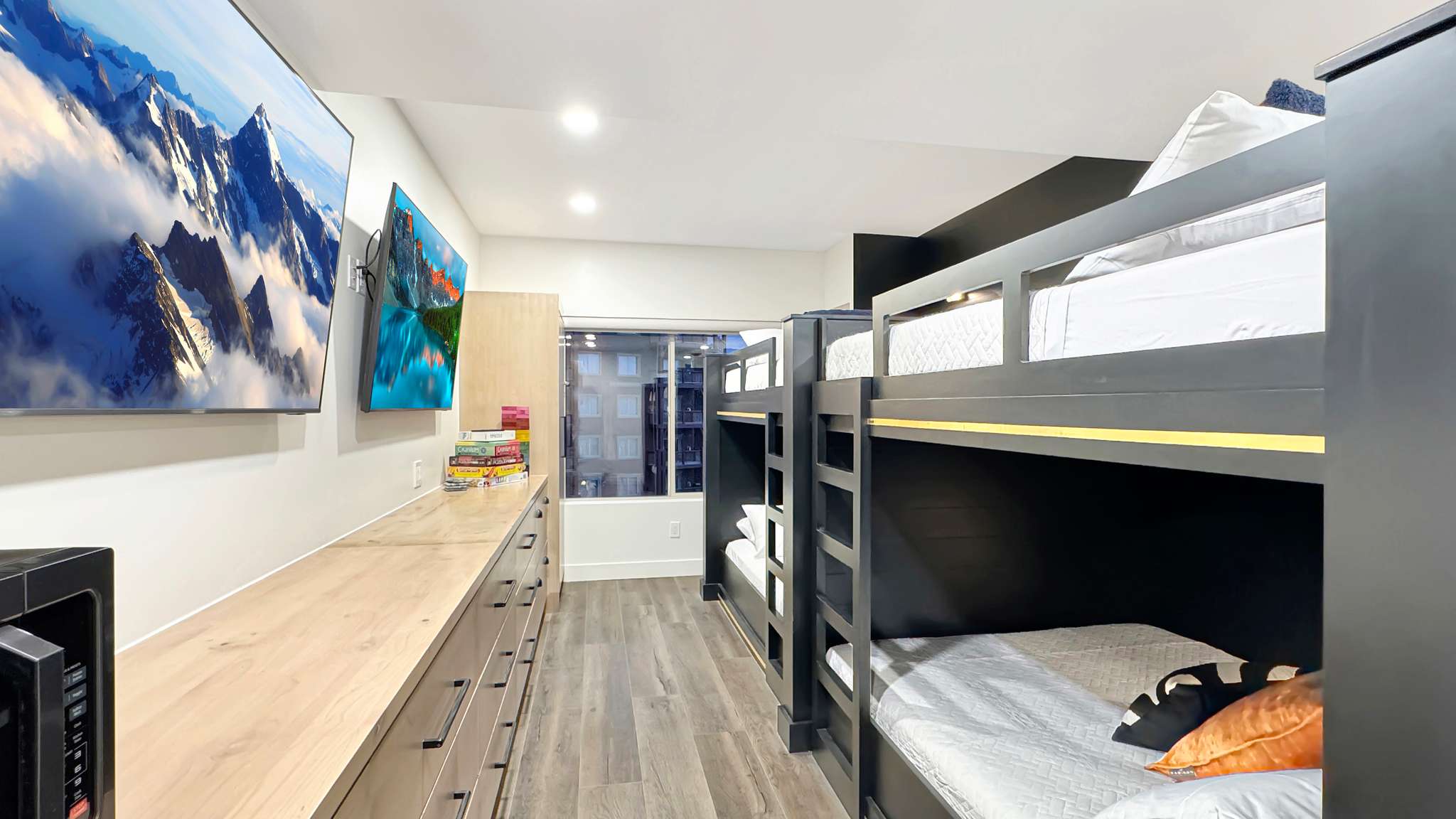 Room featuring multiple built-in bunk beds with black frames, wood-finish flooring, recessed ceiling lighting, and a window providing natural illumination