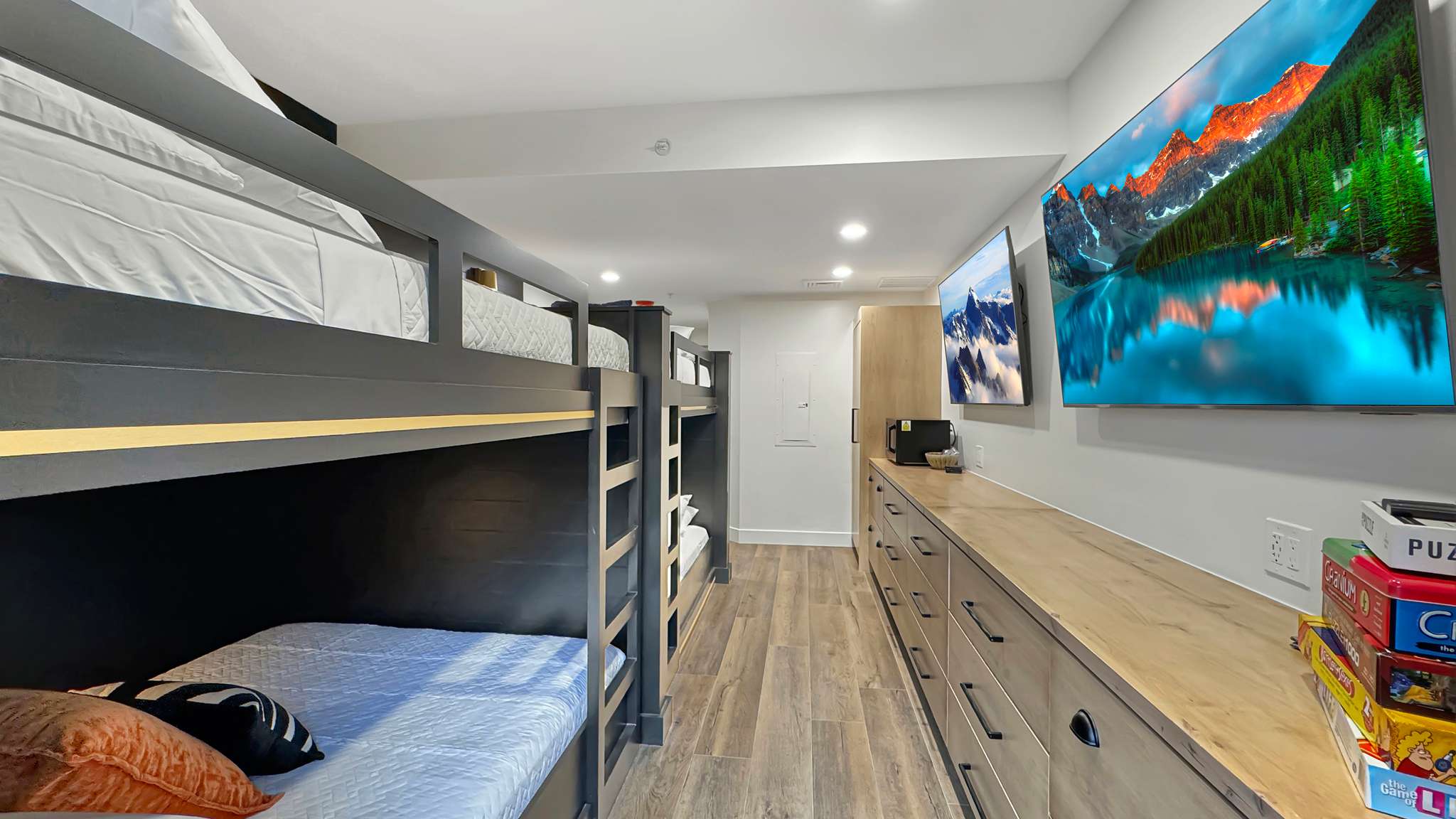 Bunk room featuring built-in bed frames, recessed lighting, wood-finish flooring, two wall-mounted televisions, and extensive built-in storage cabinetry with a wood-finish countertop