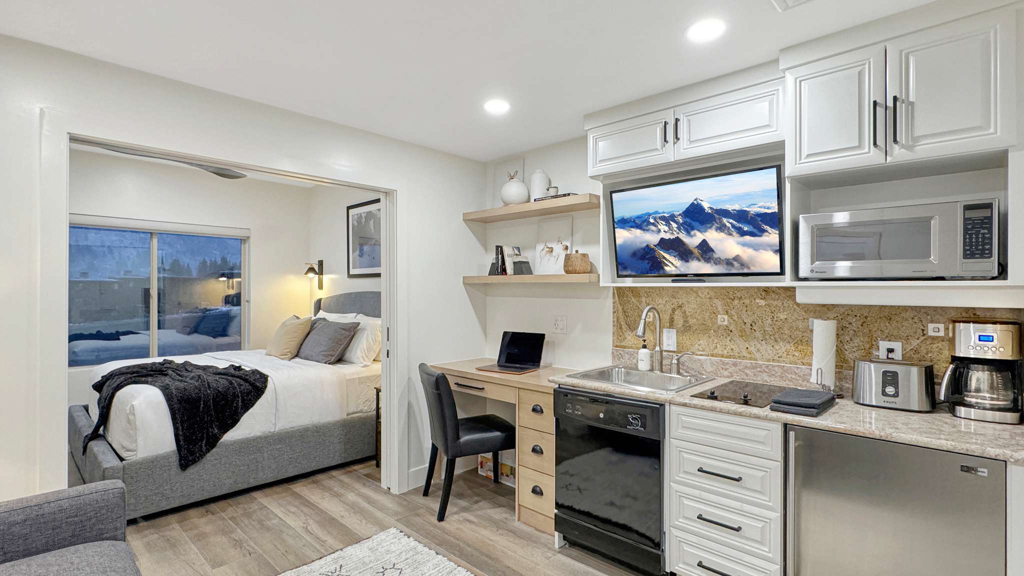 Compact kitchen area featuring white cabinetry, a built-in microwave, a stainless steel sink with a gooseneck faucet, and stone-finish countertops with a matching backsplash