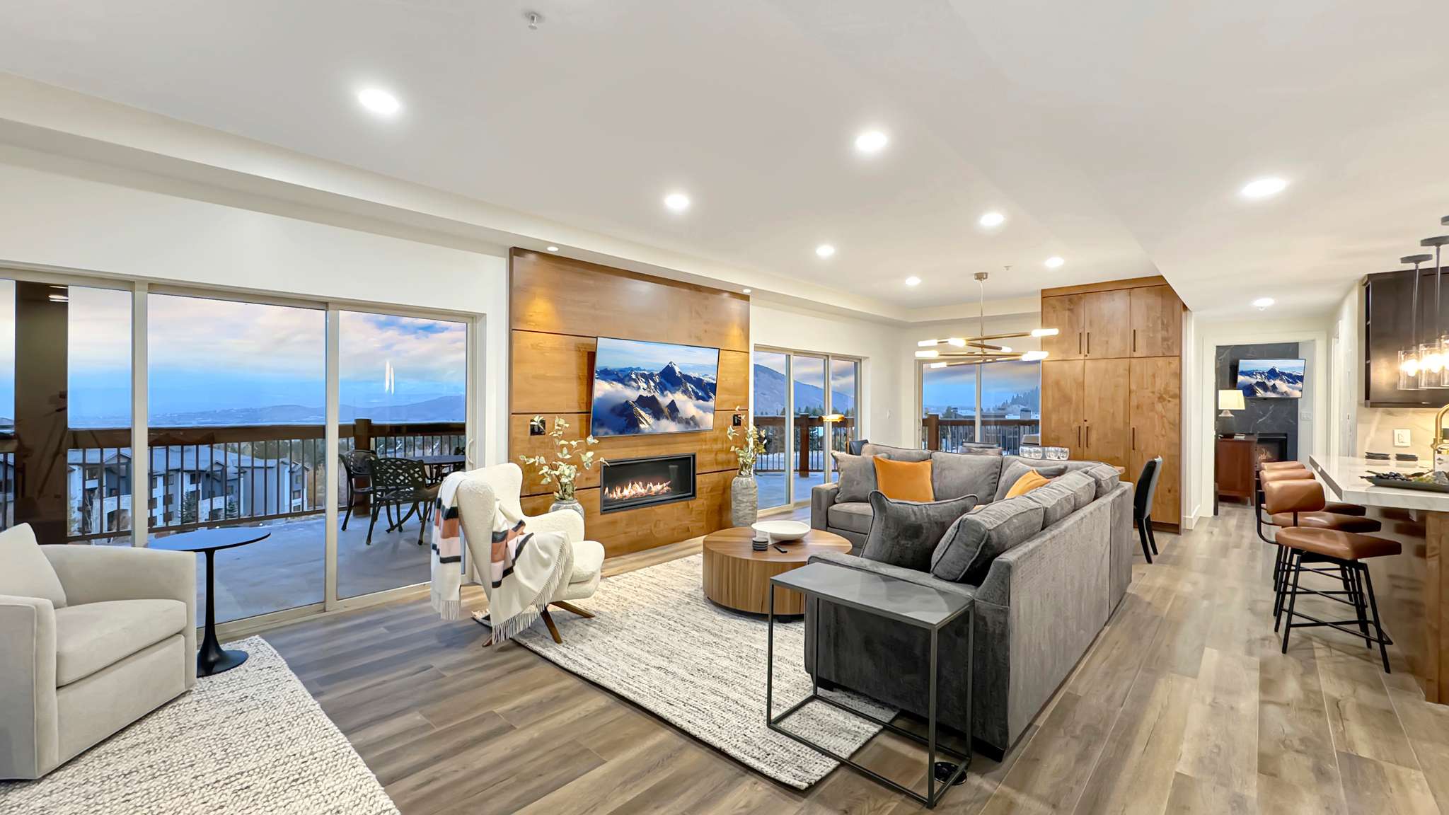 Open-concept living area featuring wood-finish flooring, a contemporary fireplace with a wood-paneled accent wall, recessed lighting, and sliding glass doors opening to a deck