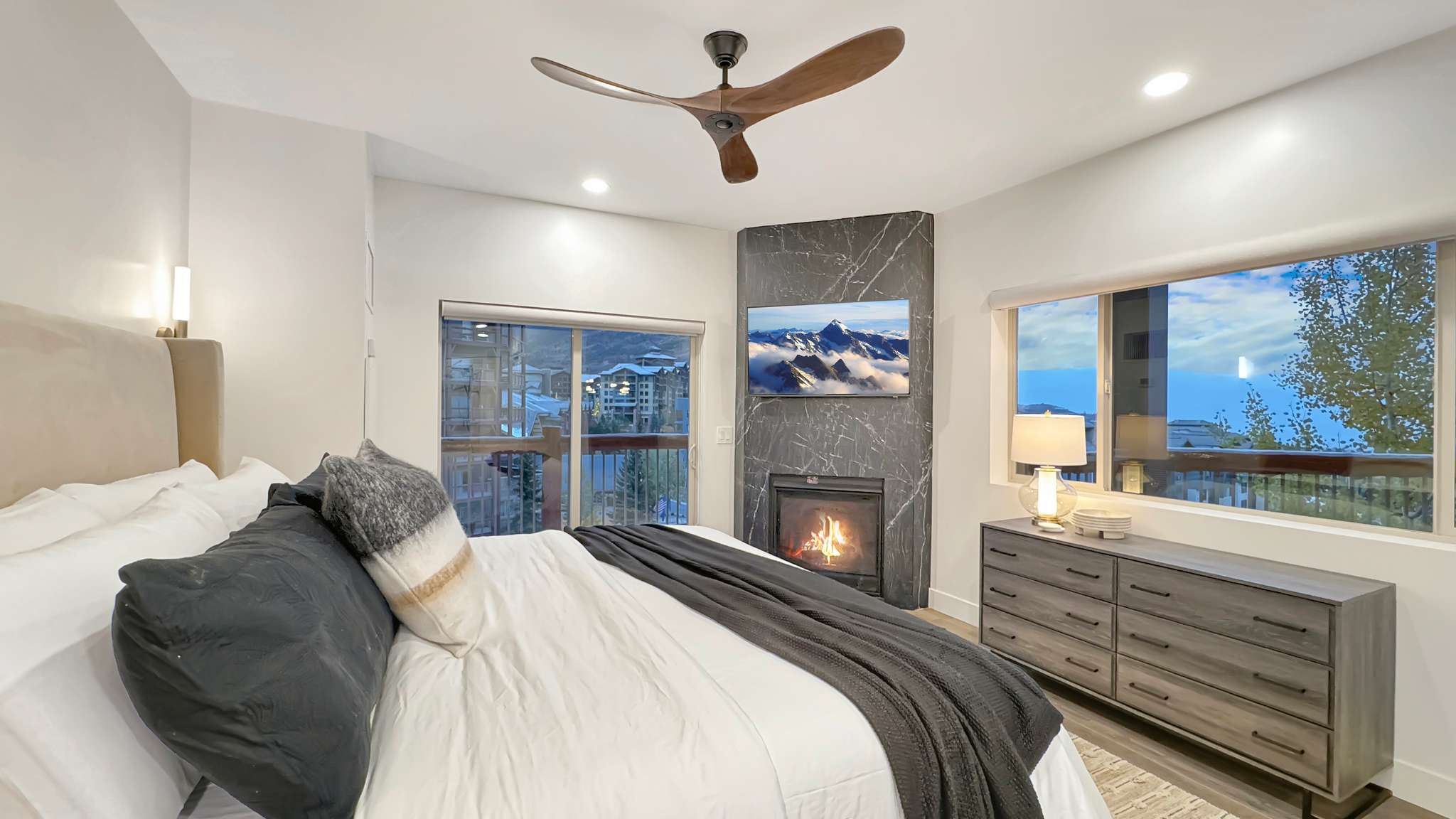 Recessed lighting illuminates this room featuring a ceiling fan with wood-finish blades, a built-in fireplace with a stone-finish surround, and a sliding glass door leading to a balcony