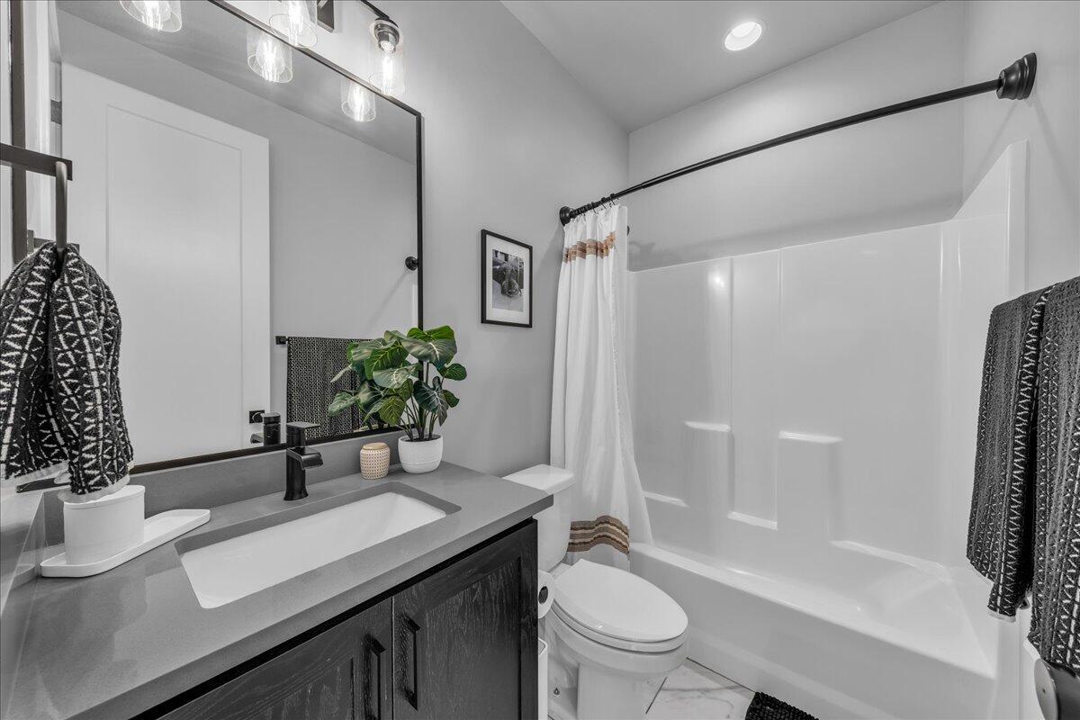 Contemporary bathroom featuring a dark wood-finish vanity with an integrated sink, a large framed mirror, and a full bathtub with a shower kit