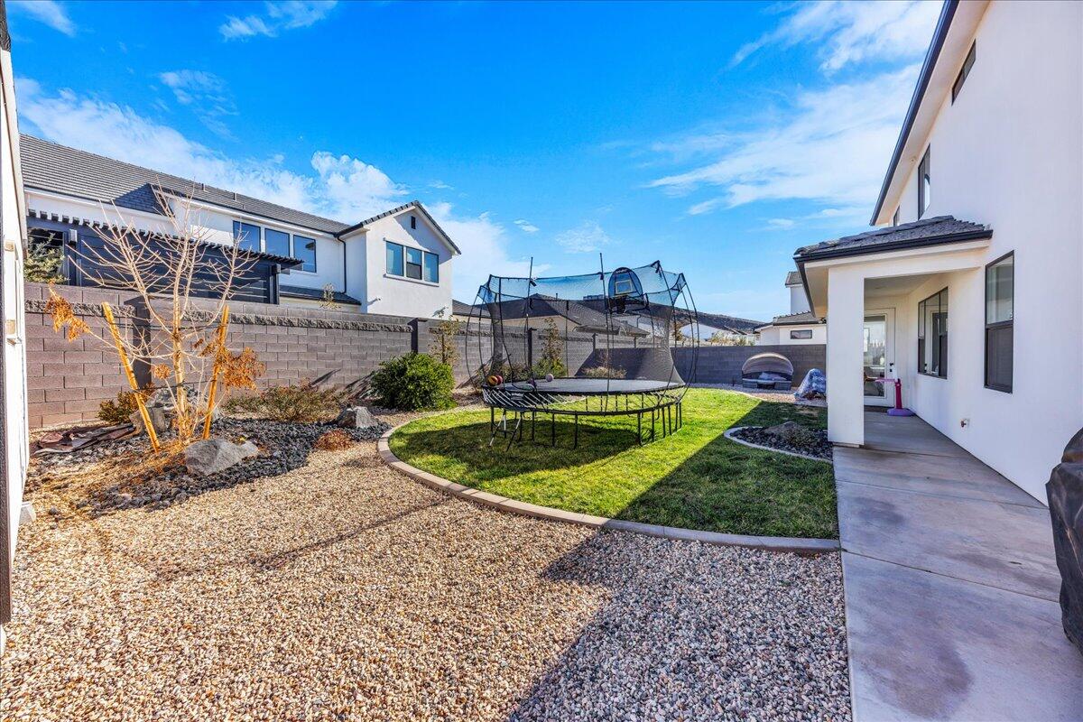 Spacious backyard featuring a manicured lawn, gravel landscaping, a concrete patio, and block perimeter fencing