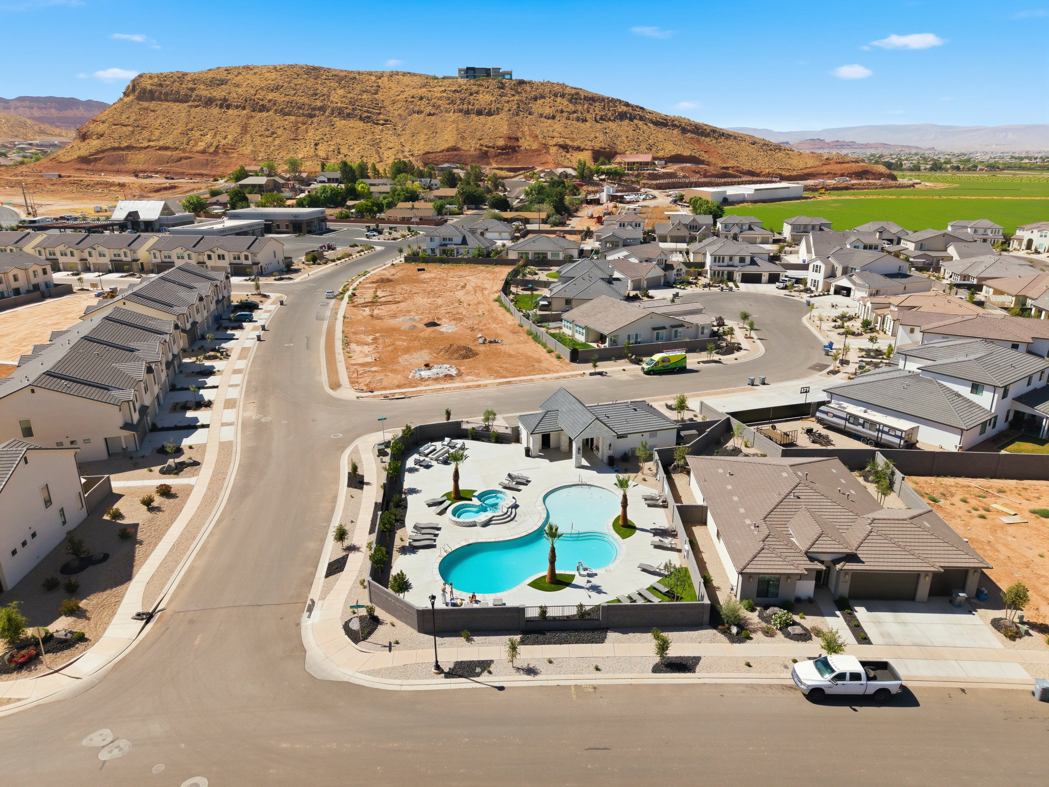 Aerial perspective of a residential community featuring a curvilinear swimming pool with an integrated spa, surrounded by lounge seating and palm trees