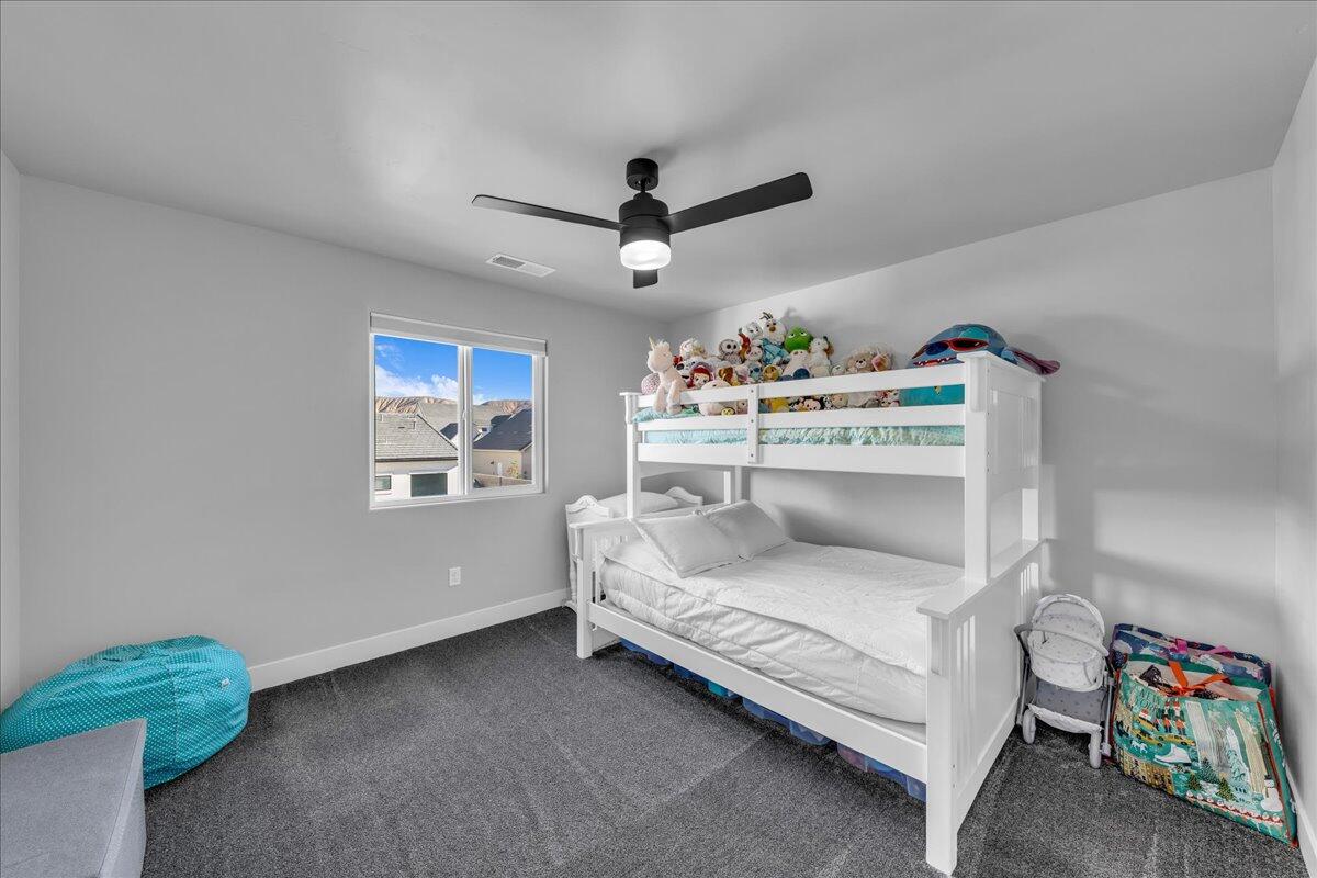 Room featuring a window, dark gray carpeting, light gray walls, and a black ceiling fan with integrated lighting