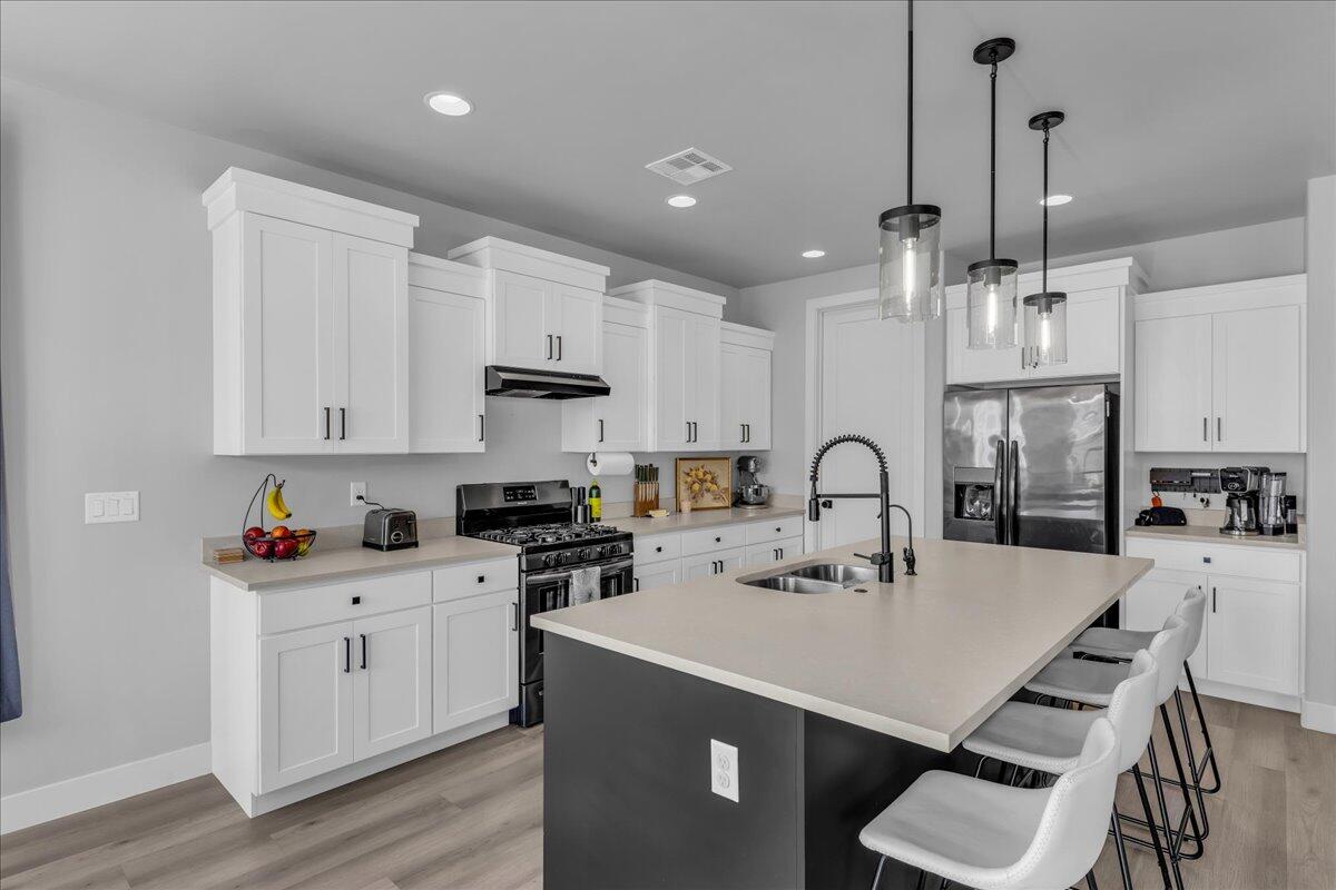 Modern kitchen featuring white shaker cabinetry, stainless steel appliances, a center island with countertop seating, and wood-finish flooring