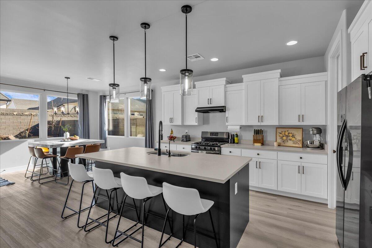 Open-concept kitchen featuring an oversized island, white shaker cabinetry, stainless steel appliances, and light wood-finish flooring