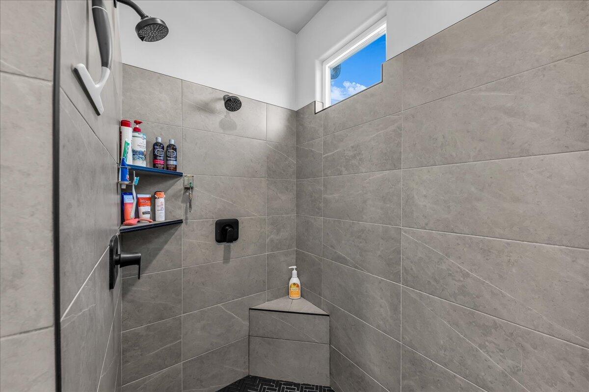 Spacious shower enclosure featuring large format grey tile walls, a built-in corner bench, and a black hexagon tile floor