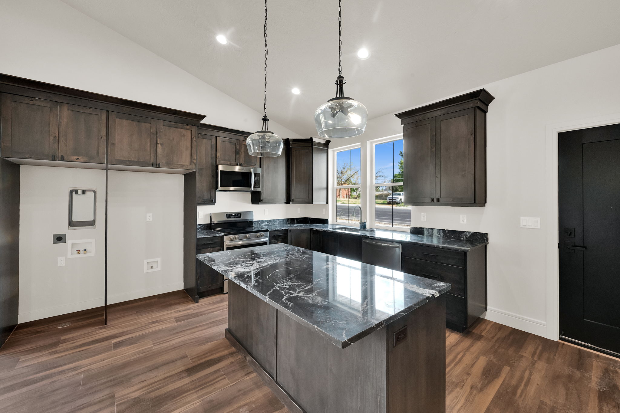 Spacious kitchen featuring an expansive island with a stone countertop, dark wood-finish cabinetry, stainless steel appliances, and wood-finish flooring