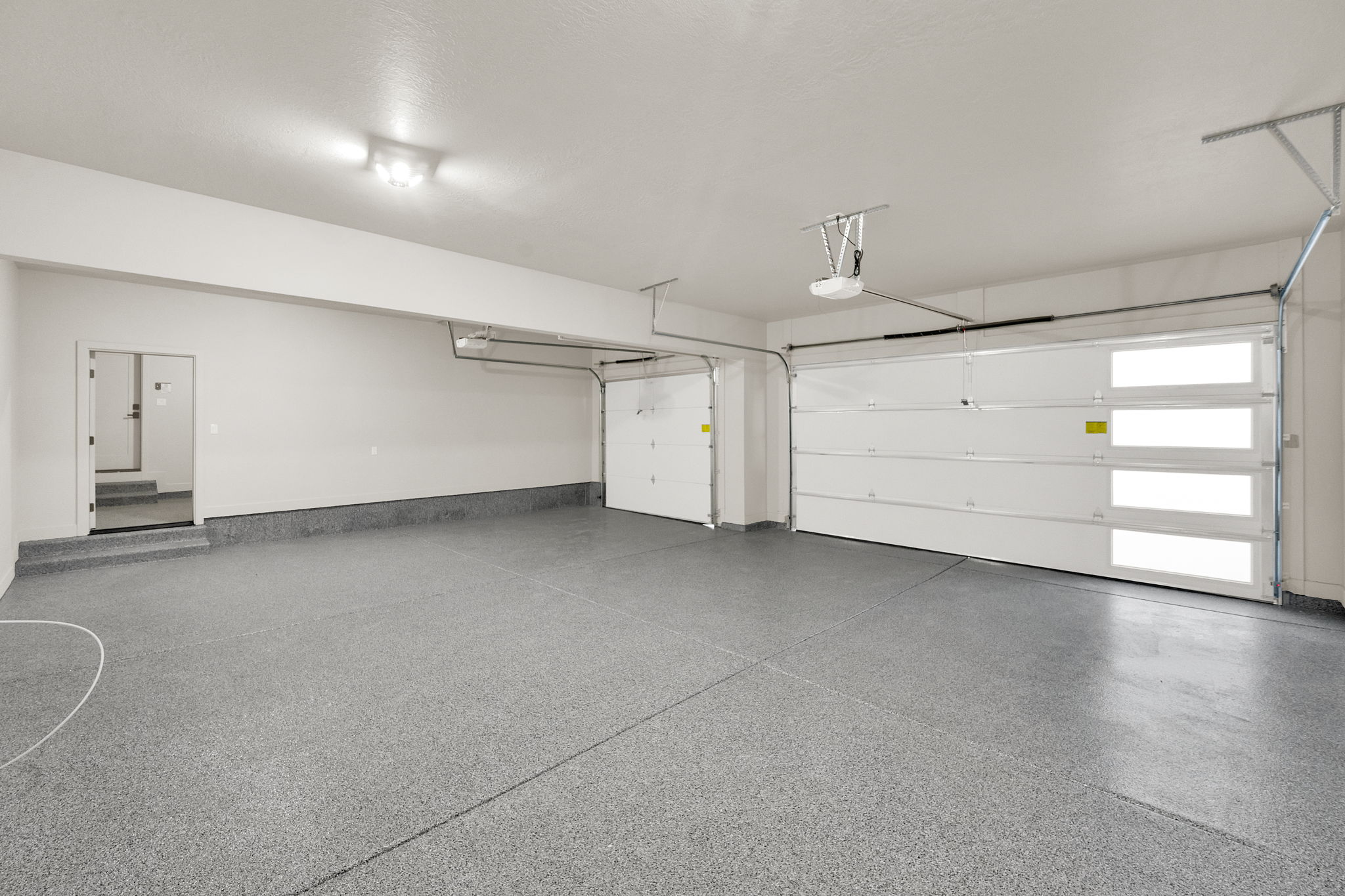 Spacious garage featuring a speckled epoxy floor coating, two overhead garage doors, and direct interior access