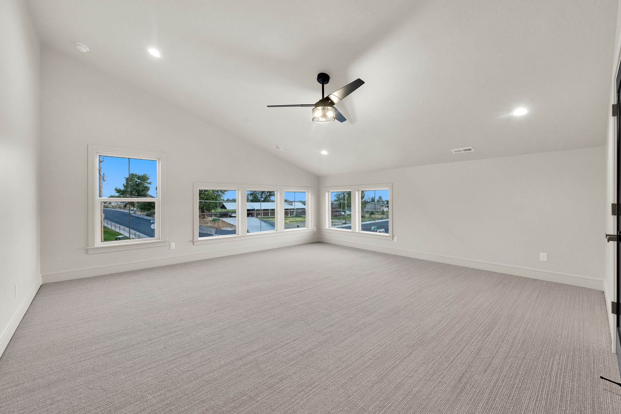 Spacious room featuring vaulted ceilings, recessed lighting, a modern ceiling fan, five windows, and light gray carpeted flooring