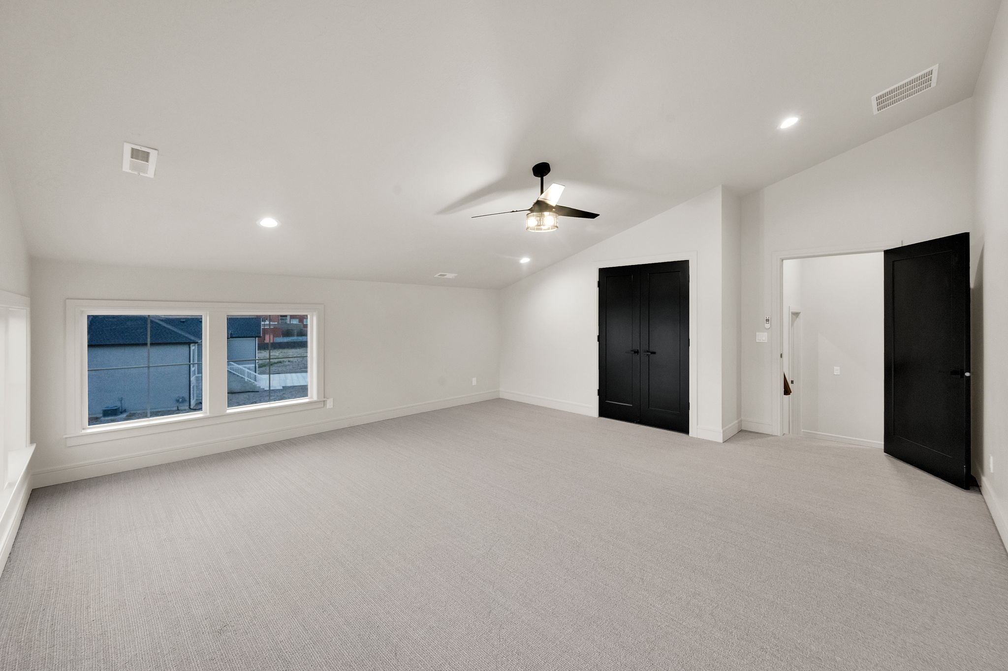 Spacious room featuring light-colored carpeting, multiple recessed lights, and a ceiling fan