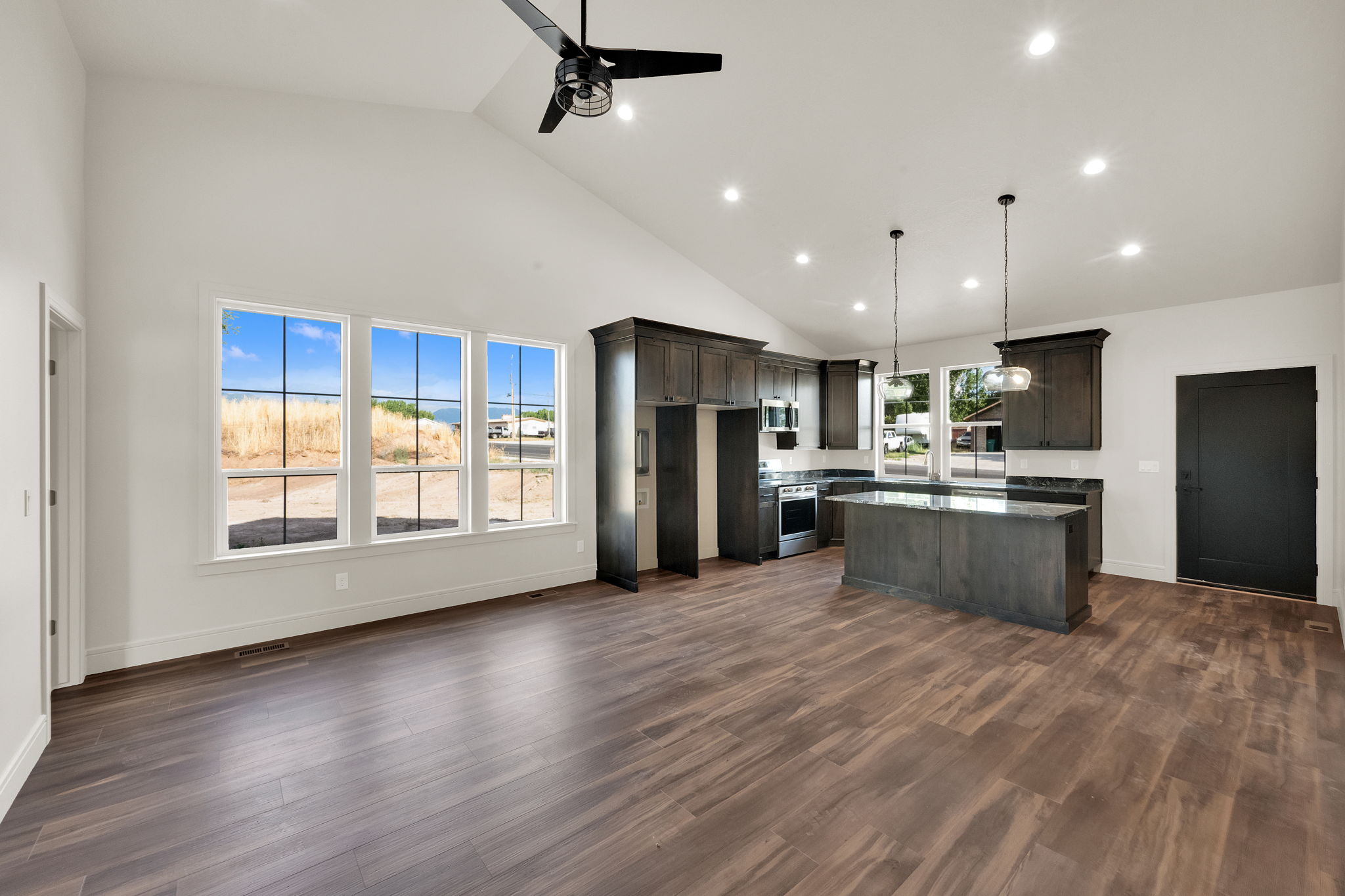 Vaulted ceiling great room featuring dark wood-finish flooring, a kitchen island with pendant lighting, recessed lighting, and a contemporary ceiling fan