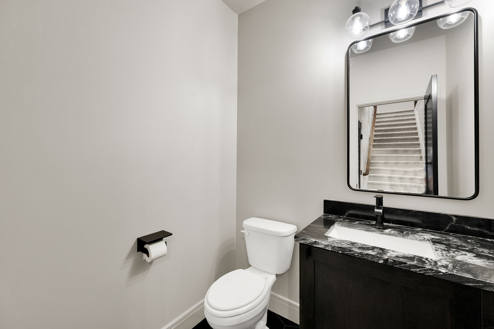 Bathroom featuring a vanity with dark cabinetry, black and white patterned countertop, undermount sink, and a black framed mirror
