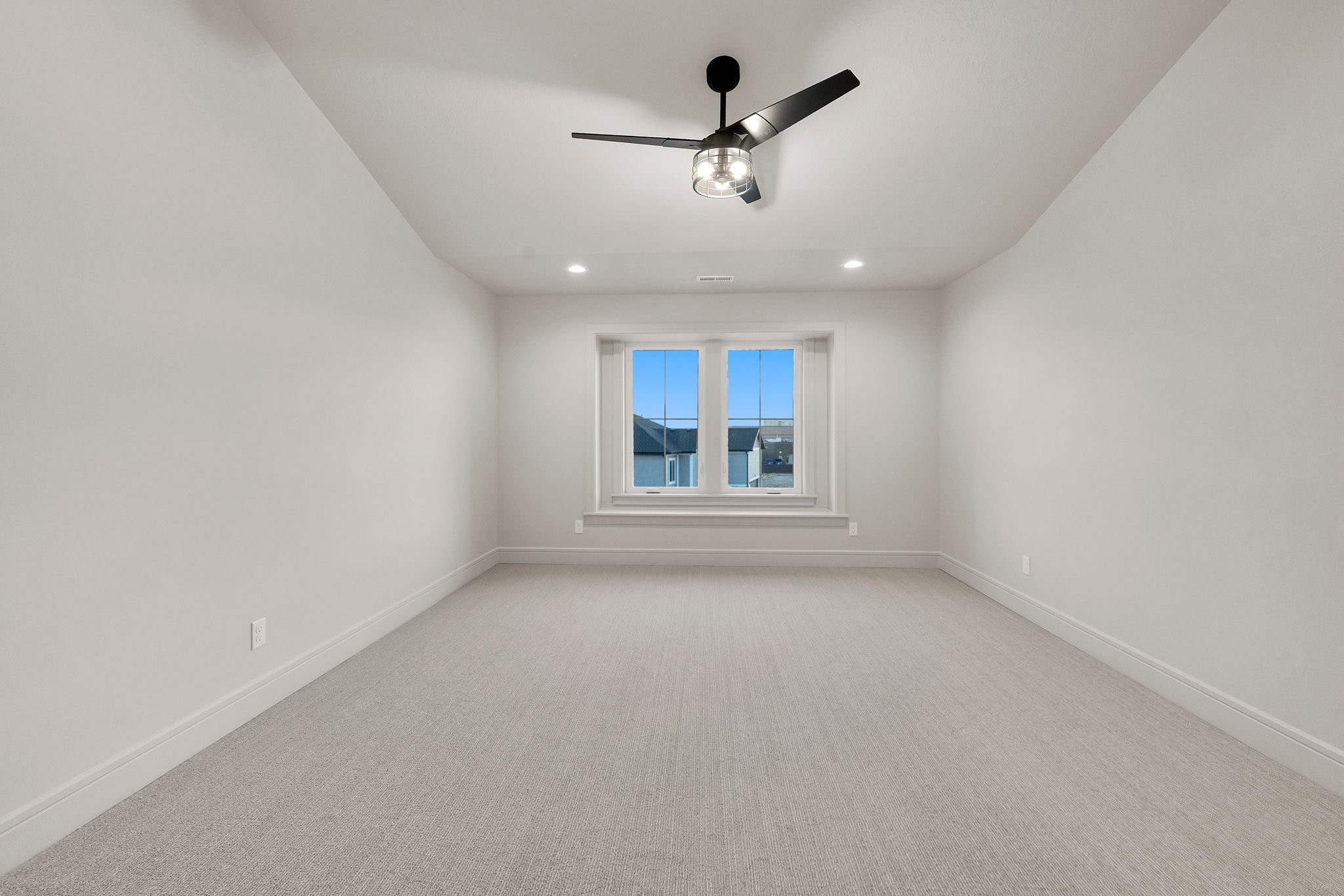 Spacious room featuring light-toned carpeting, a large window, a black ceiling fan, recessed lighting, and crisp white baseboards