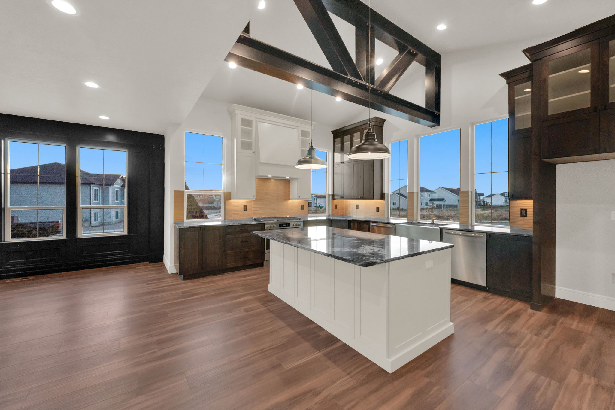 Open-concept kitchen featuring vaulted ceilings with exposed beams, wood-finish flooring, a central island with a stone countertop, white upper cabinetry, and dark lower cabinetry with stainless steel appliances