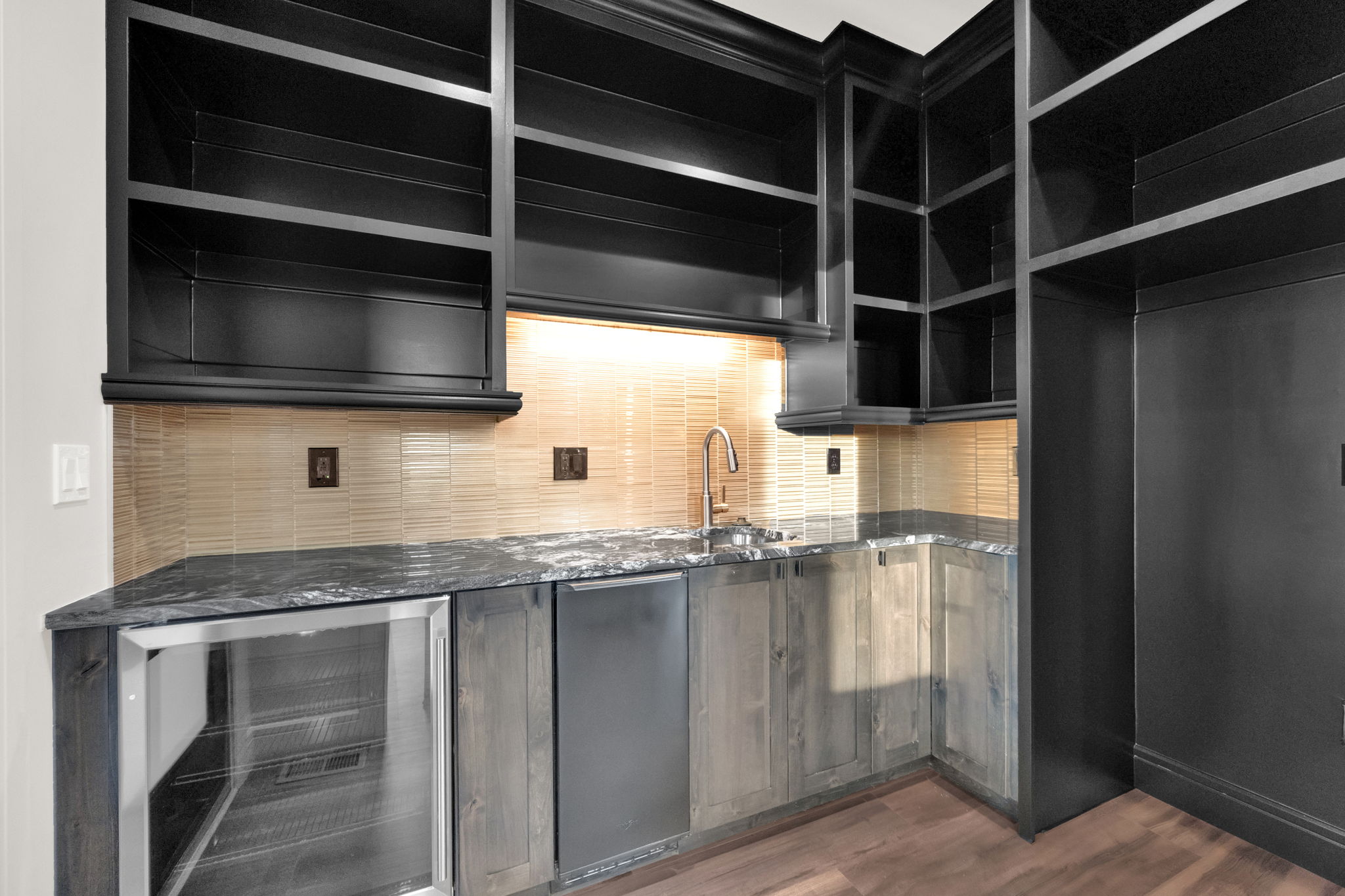 Wet bar featuring dark cabinetry, stone countertops, a tile backsplash, an undermount sink with a gooseneck faucet, and integrated beverage refrigeration