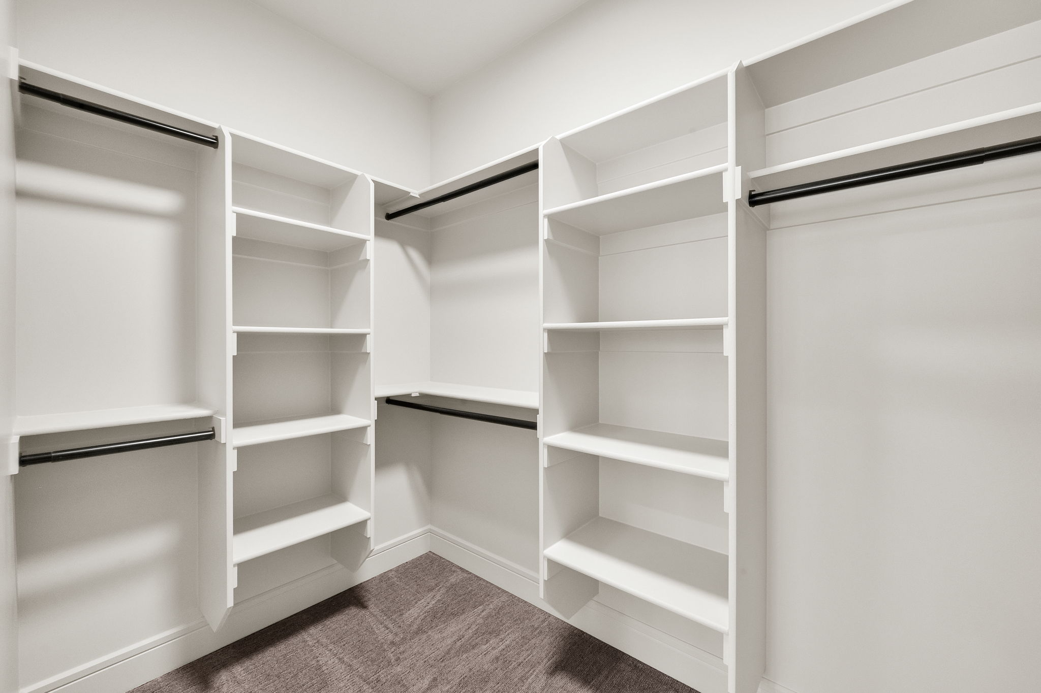 Walk-in closet featuring white built-in shelving, multiple hanging rods, and textured carpet flooring