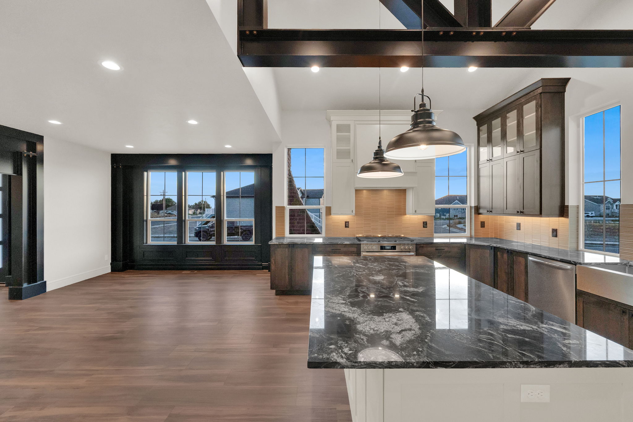 Kitchen with a large island featuring a polished dark countertop, stainless steel appliances, and industrial-style pendant lighting