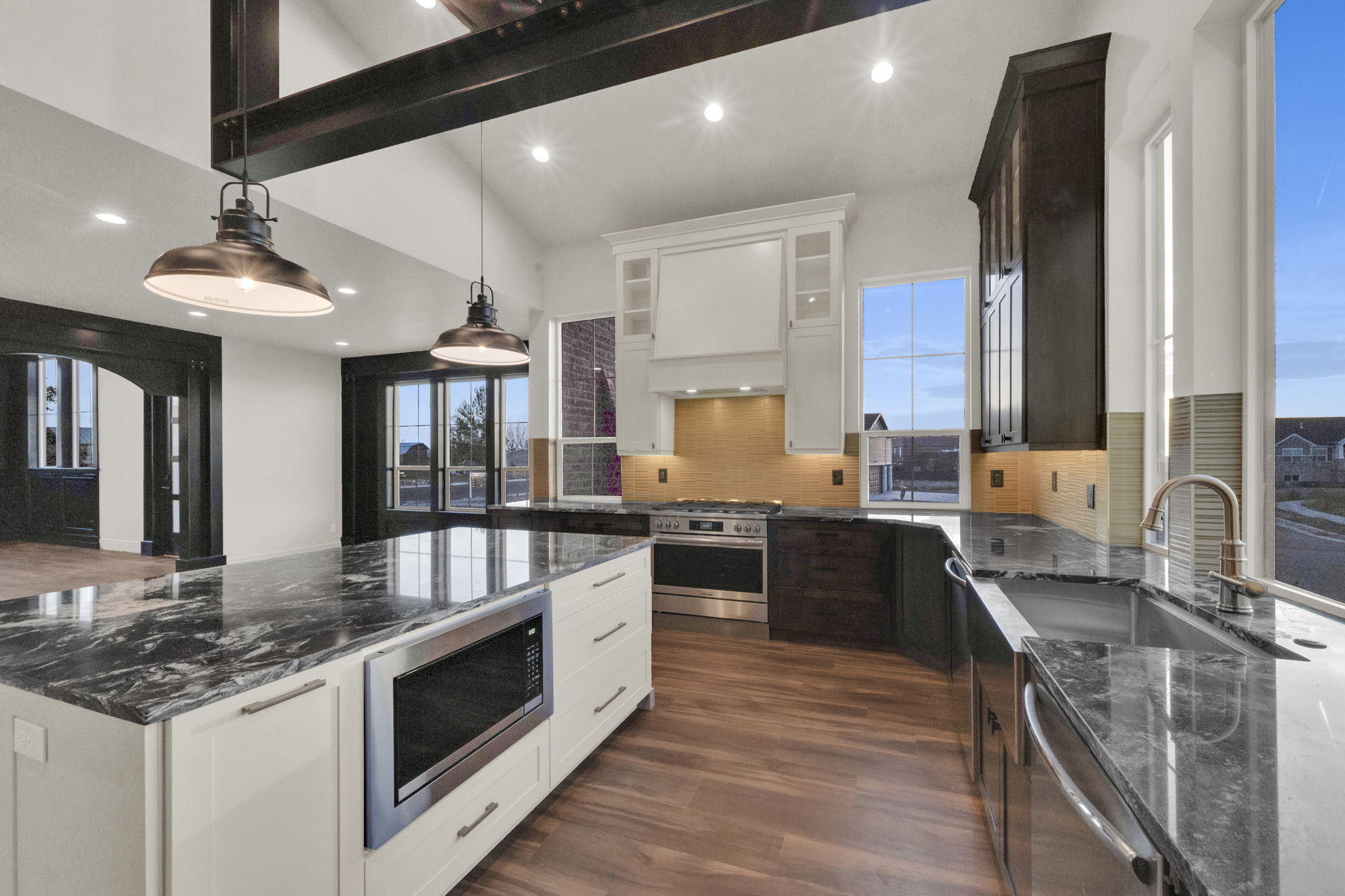Open-concept kitchen featuring an oversized island with a built-in microwave, wood-finish flooring, two-tone cabinetry, stainless steel appliances, and abundant natural light