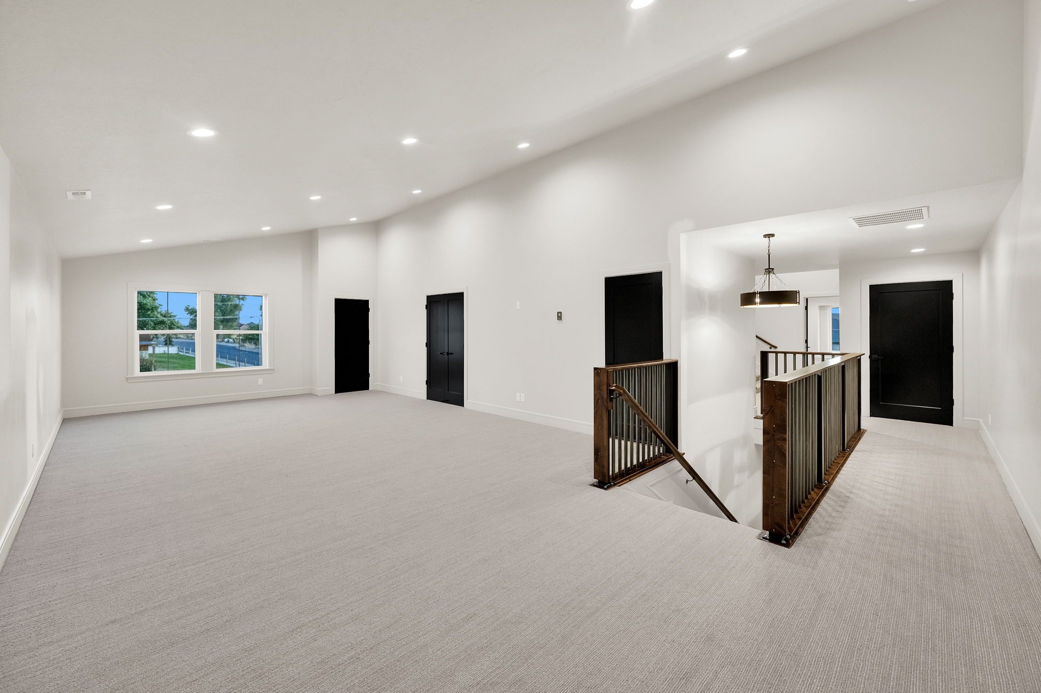 Spacious carpeted room featuring a sloped ceiling with recessed lighting, multiple windows, and dark-paneled doors