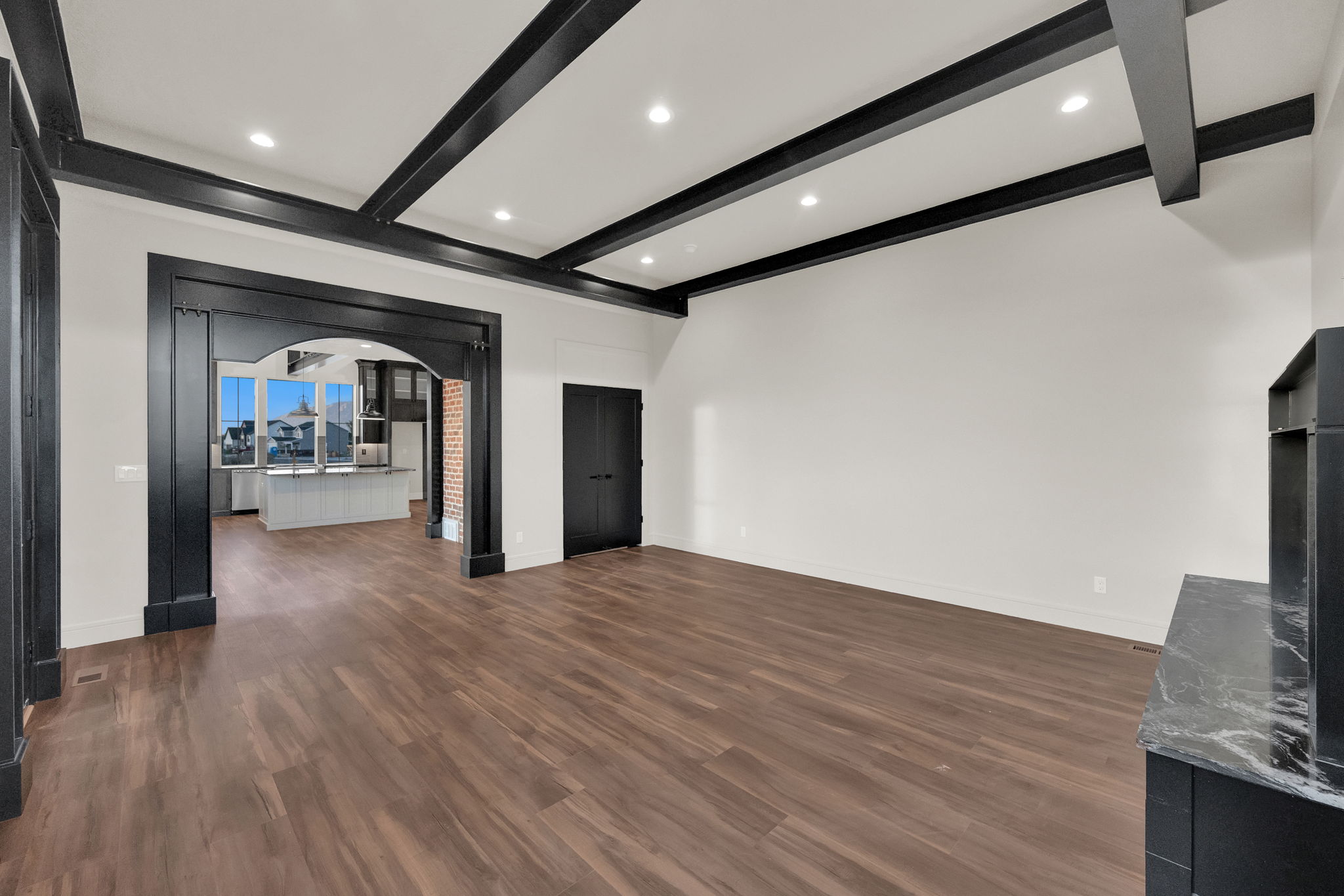 Spacious room featuring wood-finish flooring, a coffered ceiling with recessed lighting, and a decorative archway