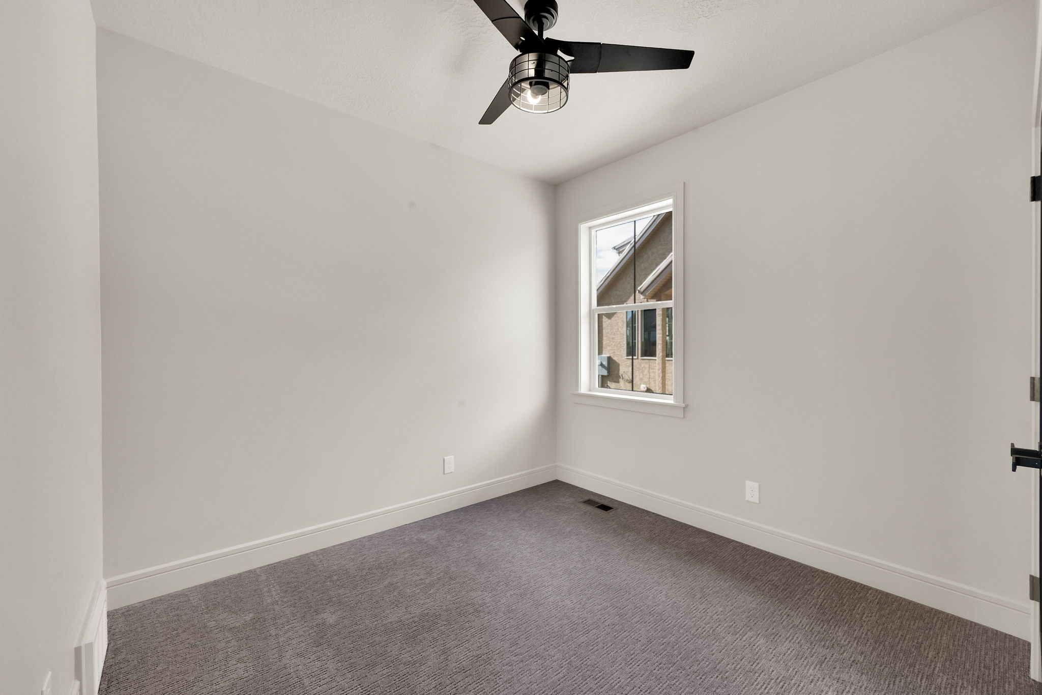 Interior room featuring neutral wall paint, gray patterned carpeting, a window with white trim, a black ceiling fan with an integrated light fixture, and white baseboards