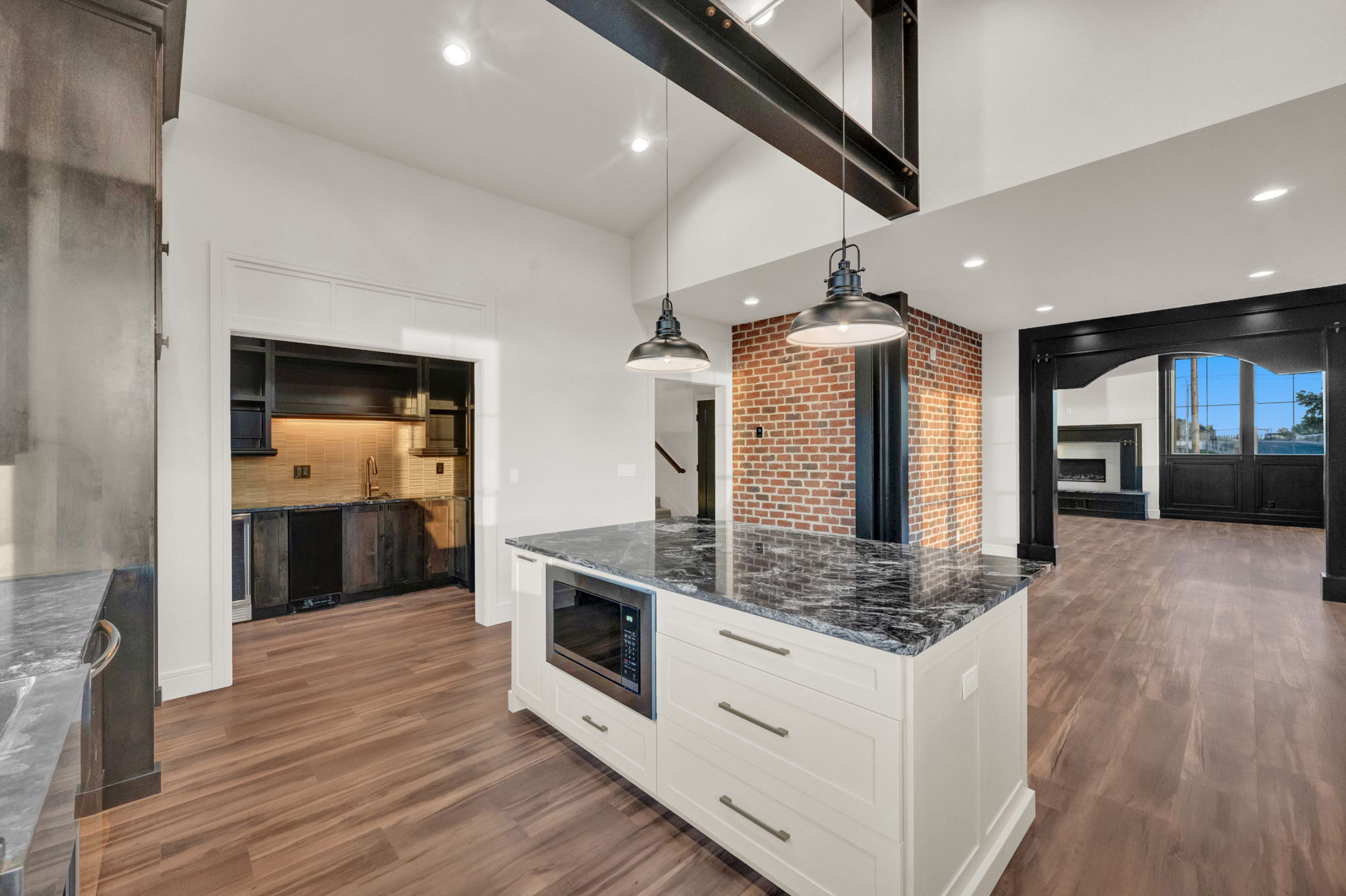 Kitchen island featuring a built-in microwave, dark granite countertop, and pendant lighting