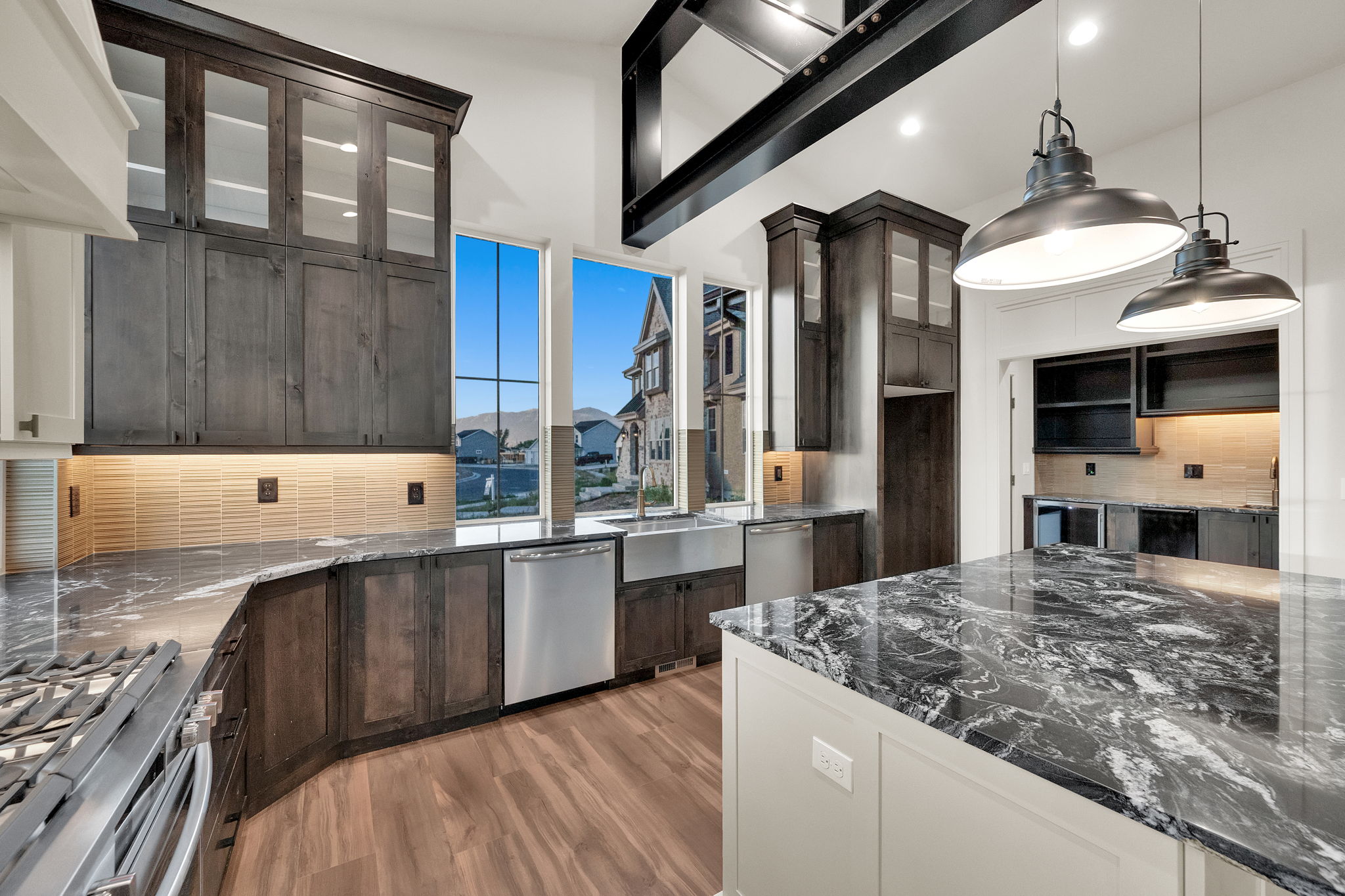 Open-concept kitchen featuring dark wood cabinetry, a large kitchen island with a stone countertop, stainless steel appliances, a tile backsplash, and wood-finish flooring