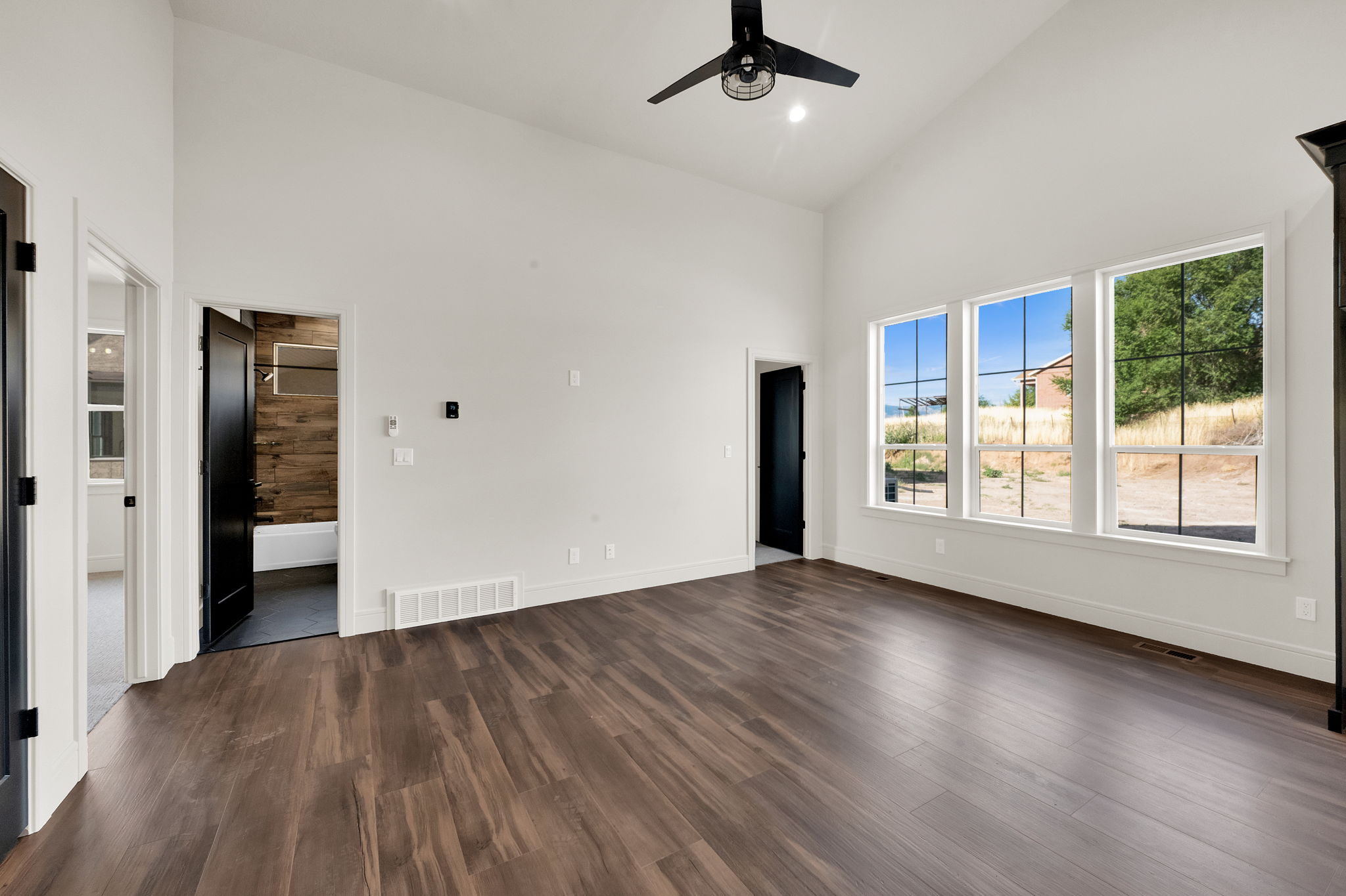 Spacious room featuring vaulted ceilings, dark wood-finish flooring, and a modern black ceiling fan