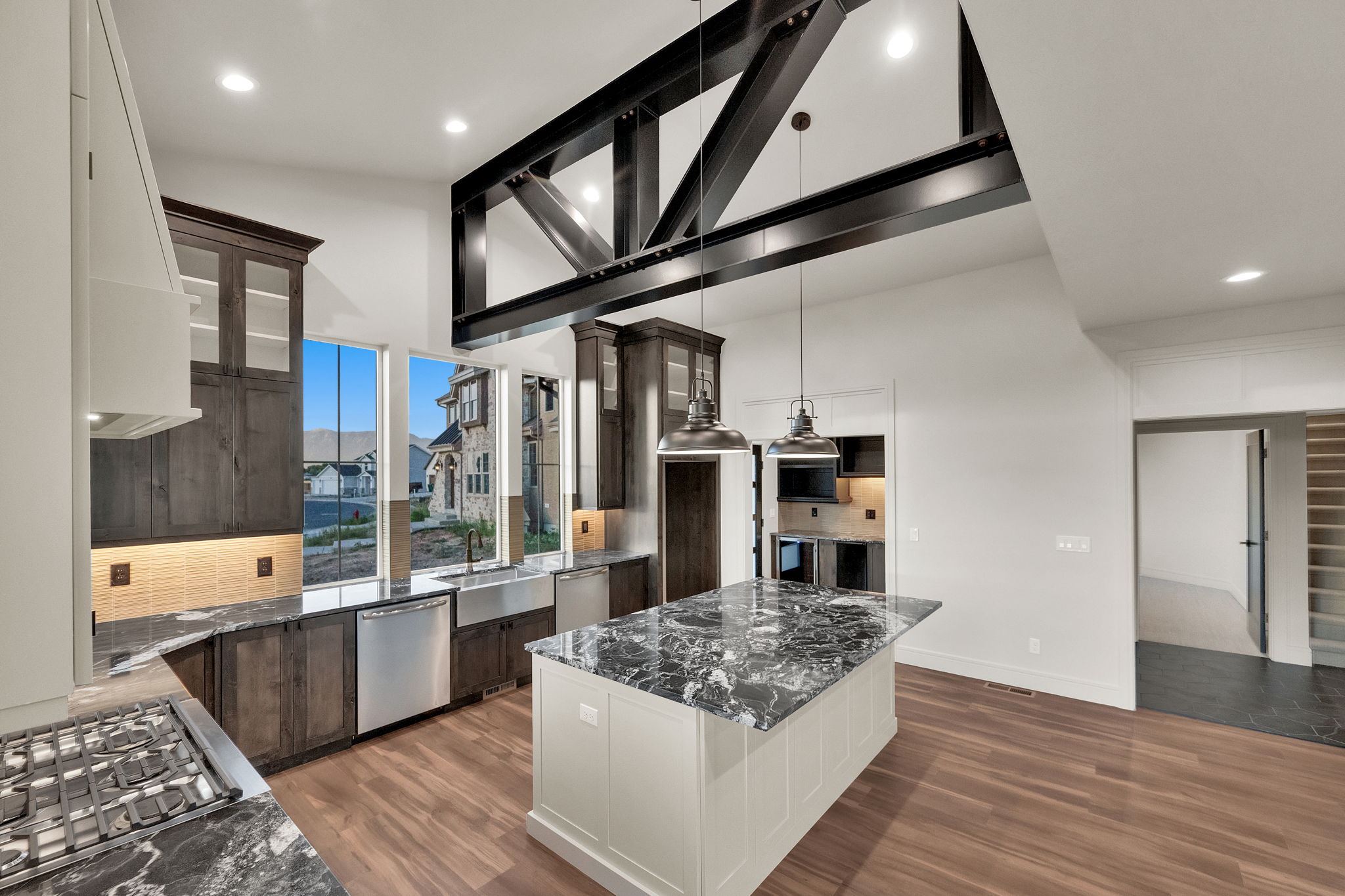Open-concept kitchen featuring a large central island with a stone countertop, vaulted ceilings with exposed dark beam work, stainless steel appliances, and wood-finish flooring
