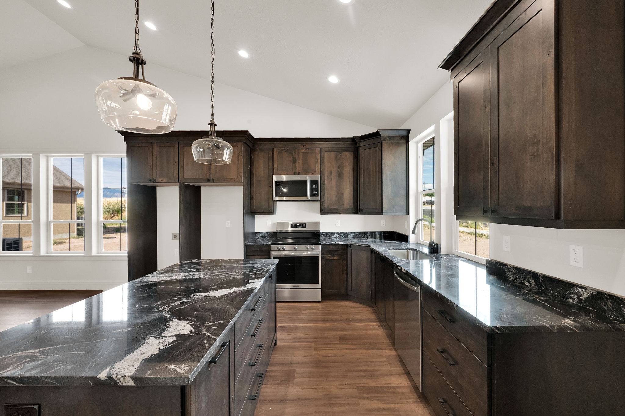 Gourmet kitchen featuring a large central island, dark wood-finish cabinetry, stainless steel appliances, vaulted ceilings, and extensive black stone countertops