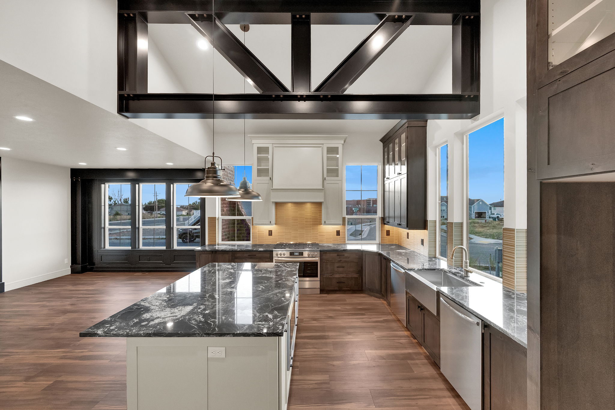 Open-concept kitchen with a large island featuring a polished granite countertop, wood-finish flooring, exposed structural beams, full-height cabinetry, and a stainless steel farmhouse sink