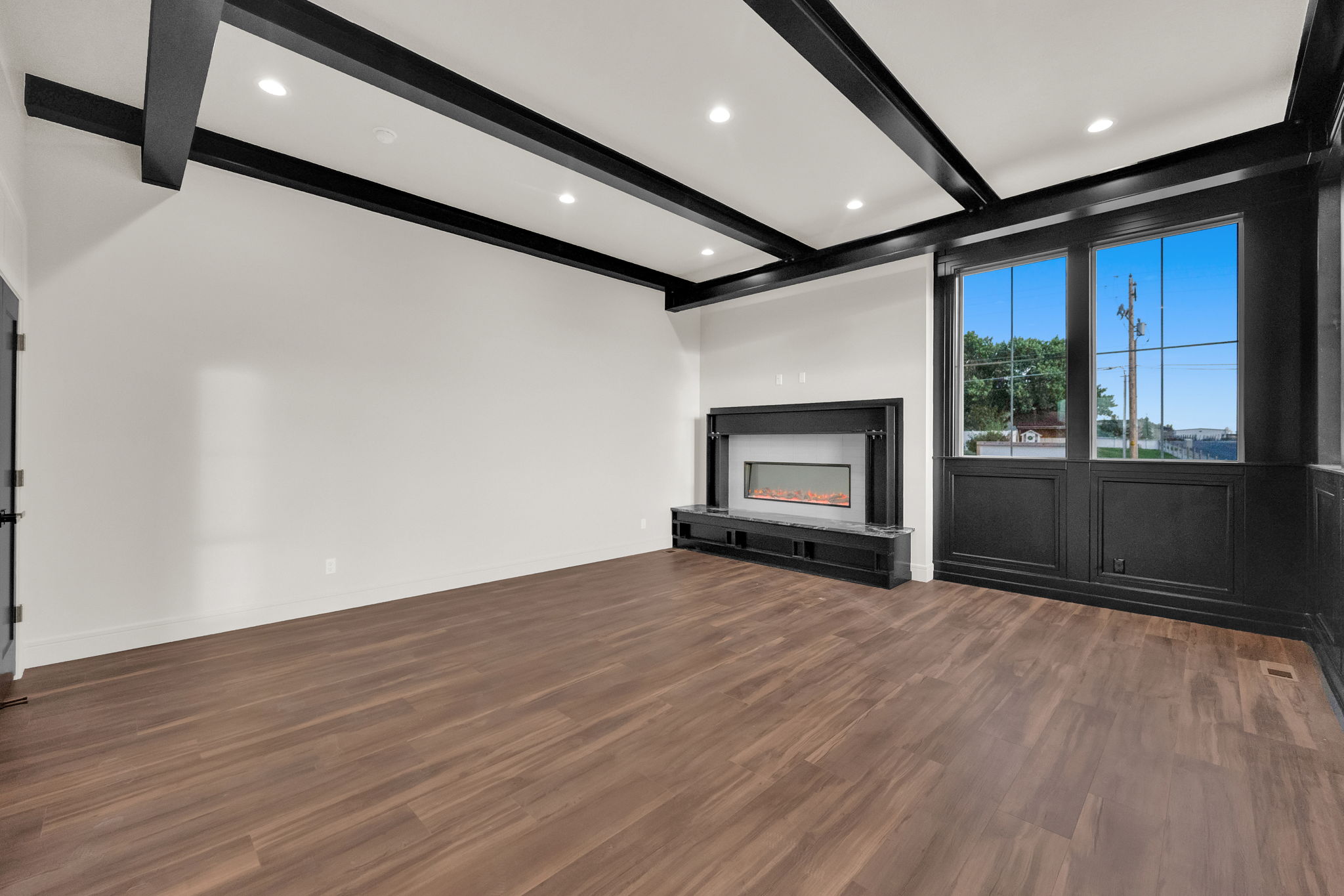Spacious interior featuring dark wood-finish flooring, a linear fireplace with a stone hearth, recessed lighting, and exposed ceiling beams
