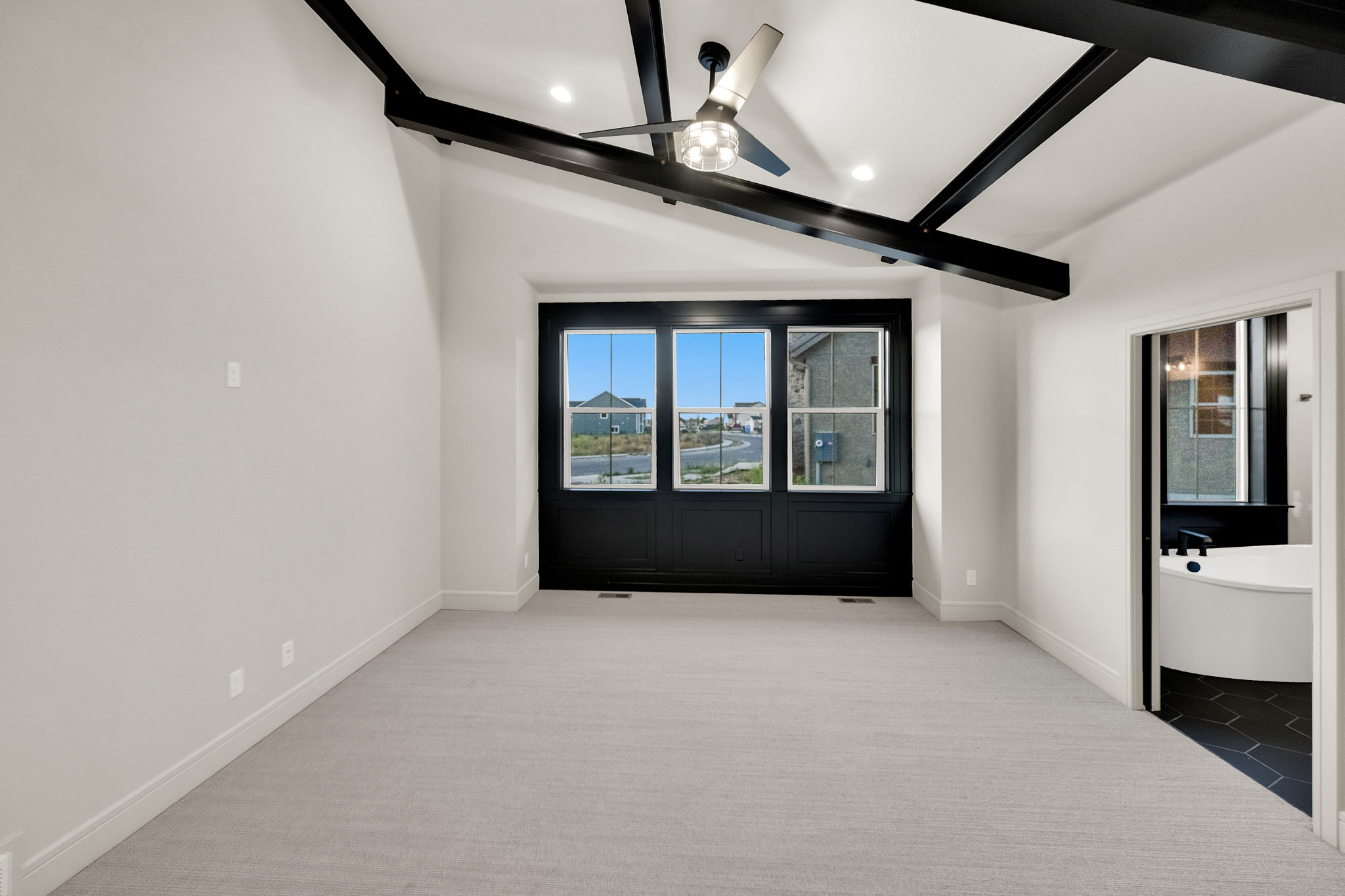 Spacious room featuring vaulted ceilings with dark wood-finish beams, a modern ceiling fan, and recessed lighting