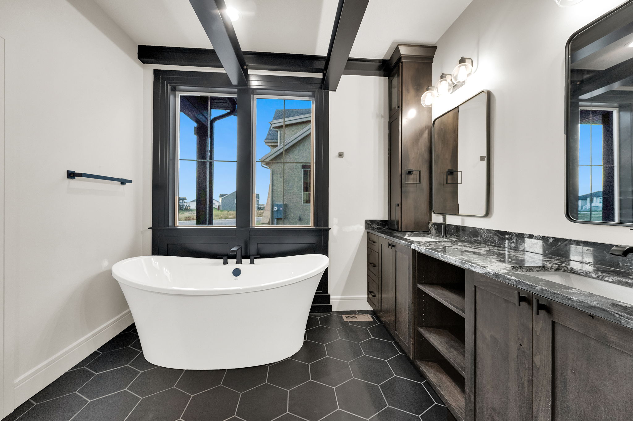 Freestanding soaking tub with black fixtures, set against black-framed windows