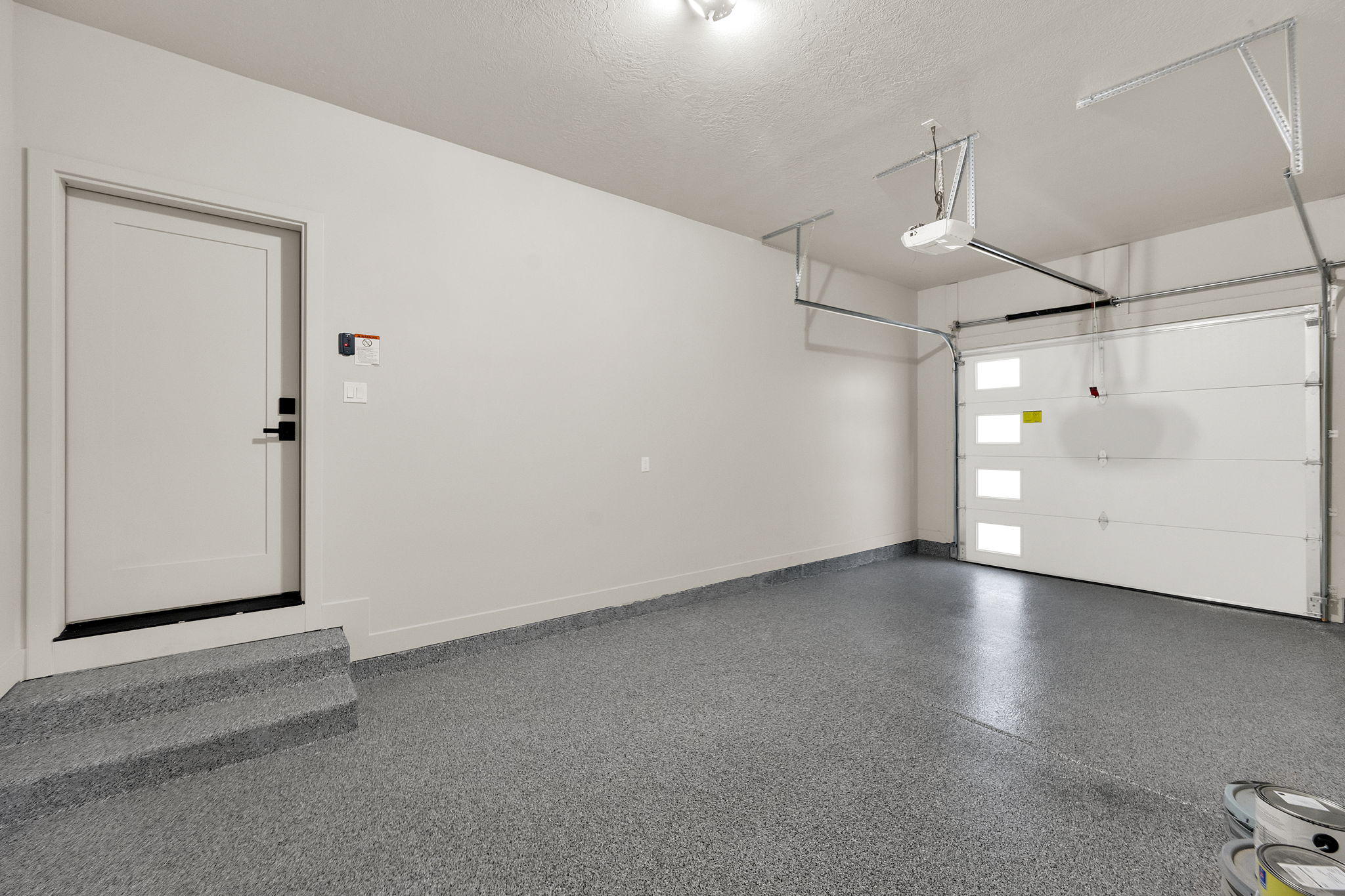 Spacious garage with an epoxy-coated concrete floor, a white paneled overhead door with frosted glass inserts, and an automatic garage door opener