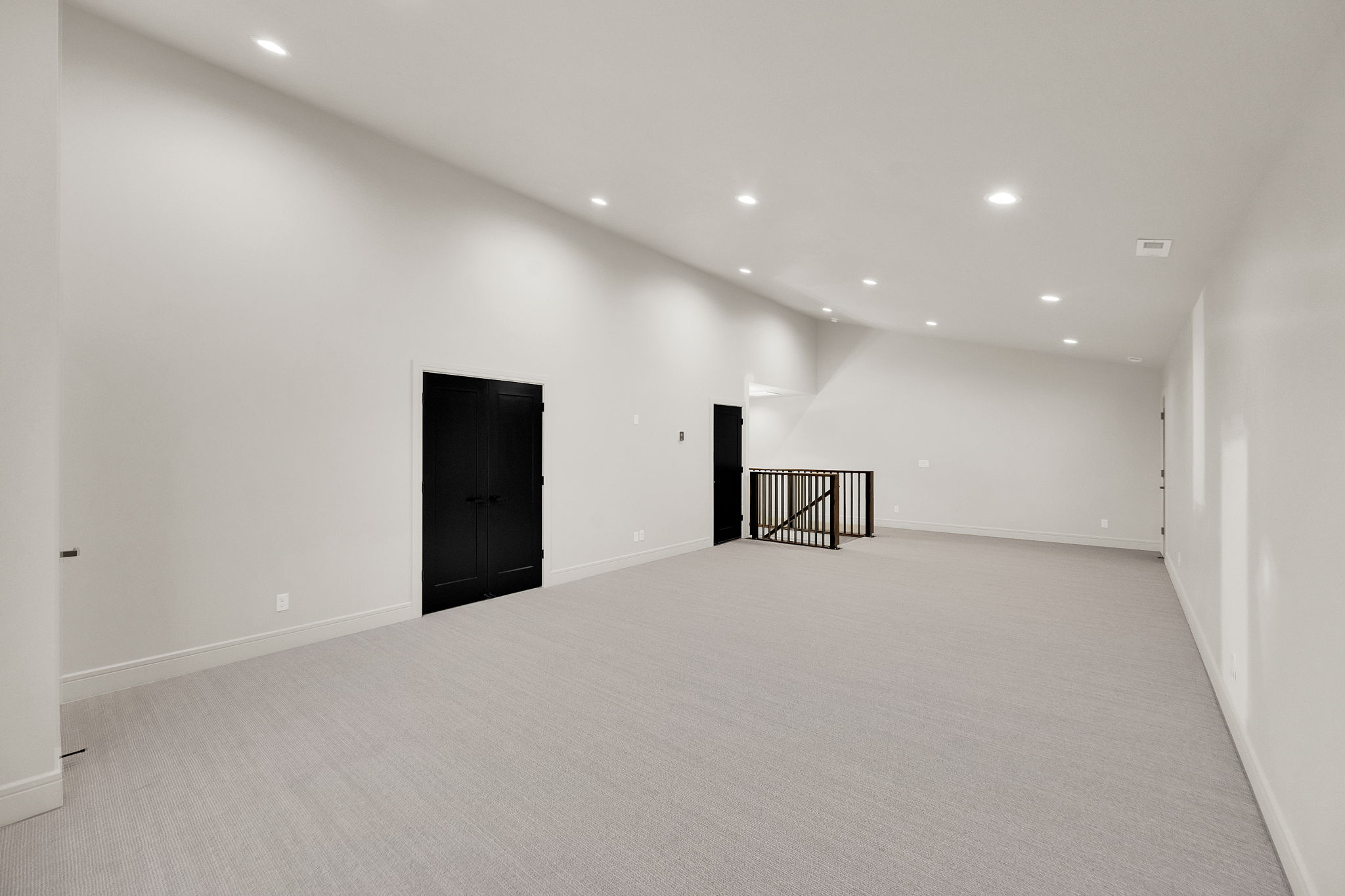 Spacious carpeted room featuring recessed lighting, a vaulted ceiling, and dark paneled double doors