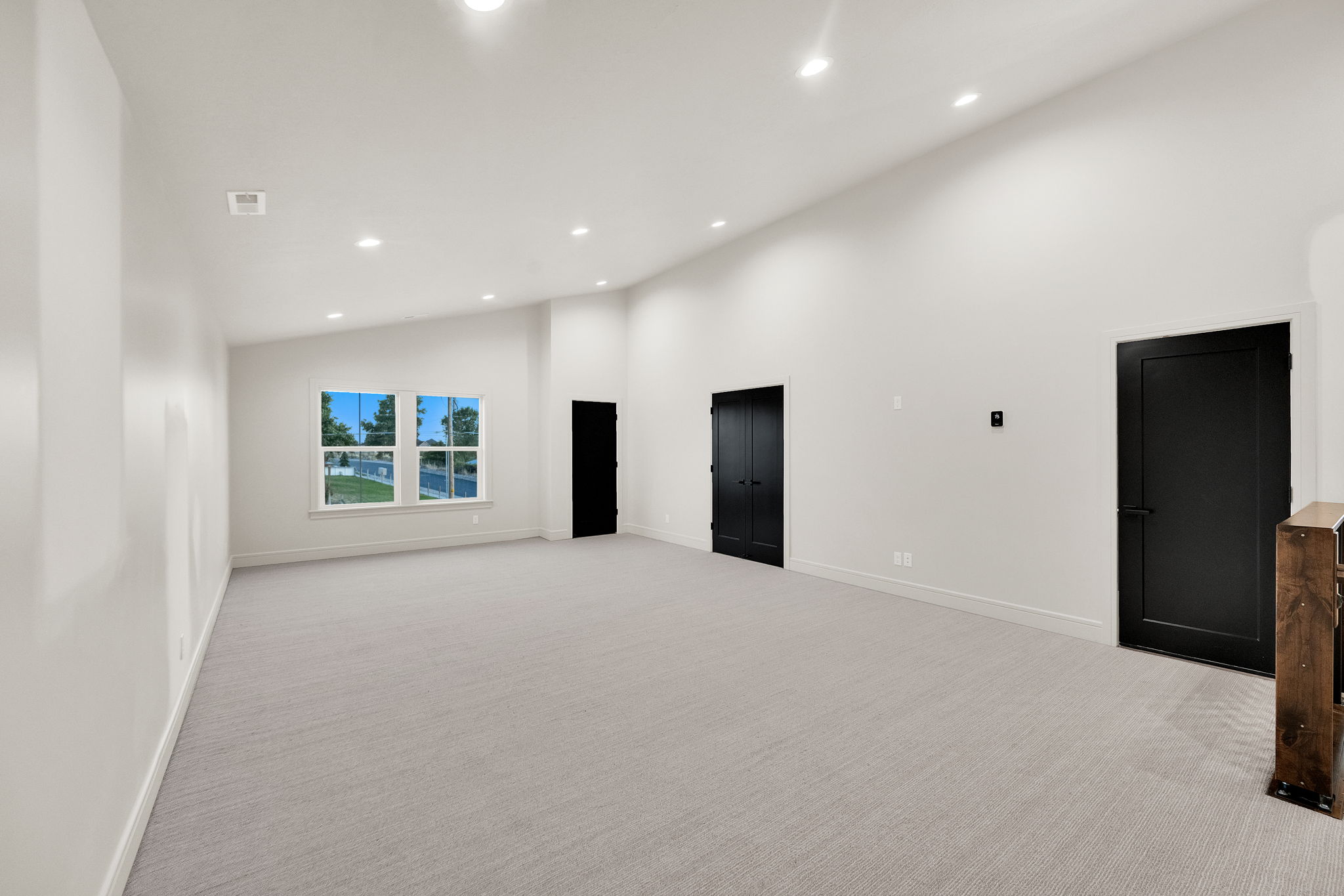 Spacious room featuring light-colored carpeting, white walls, and a vaulted ceiling with recessed lighting
