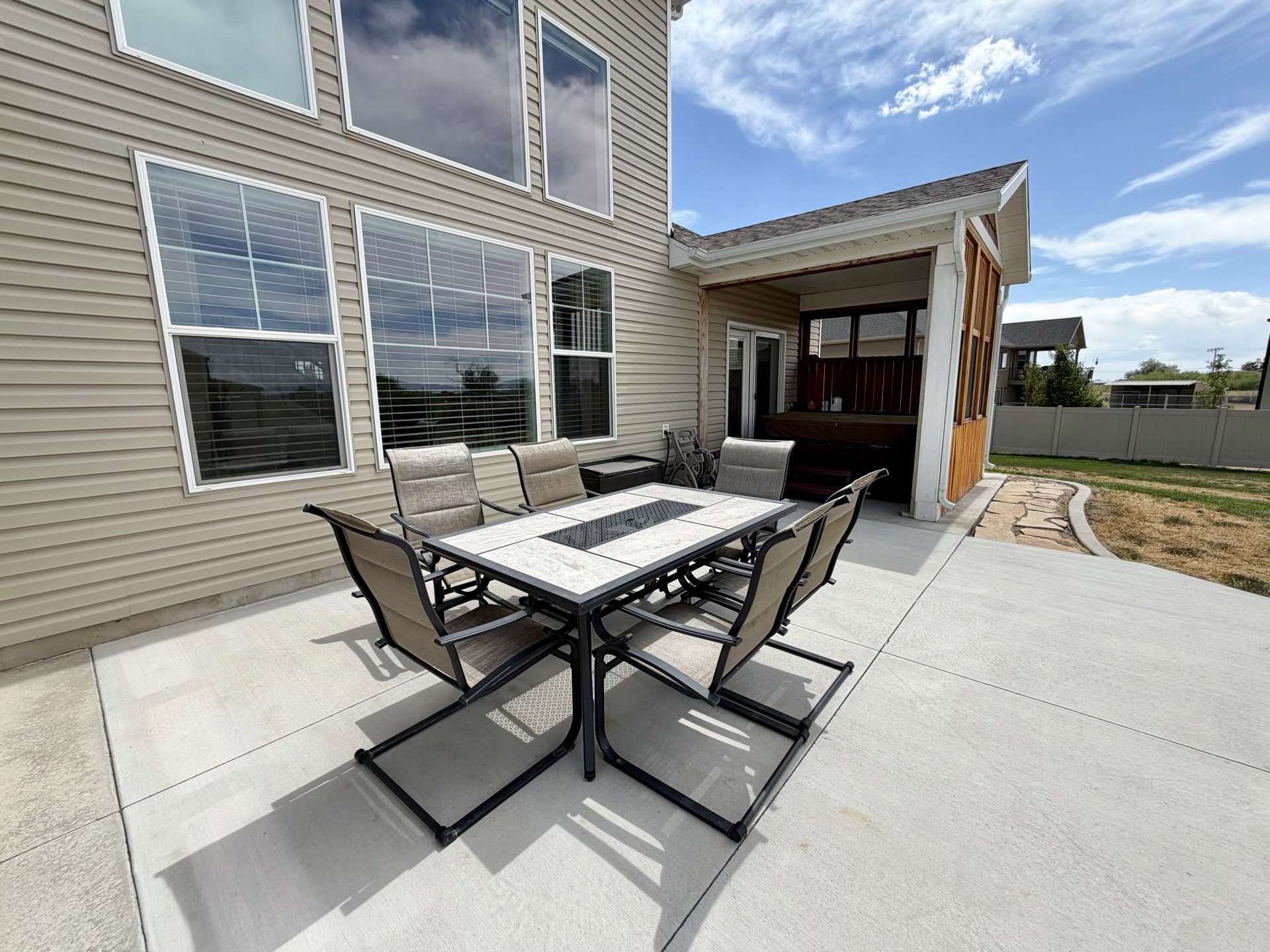 Spacious concrete patio with an adjacent covered deck, featuring siding exterior and multiple windows