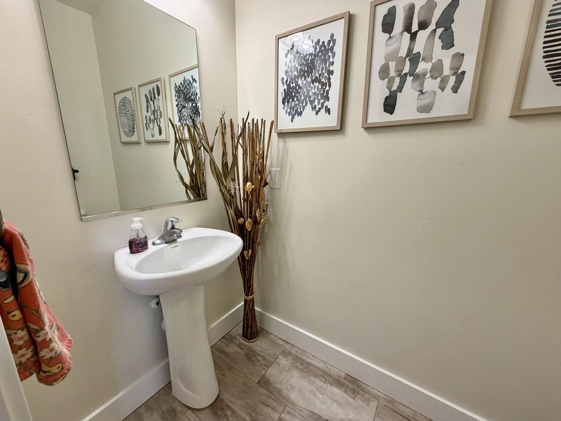 Pedestal sink with chrome faucet, large wall-mounted mirror, light-colored walls, and wood-finish tile flooring