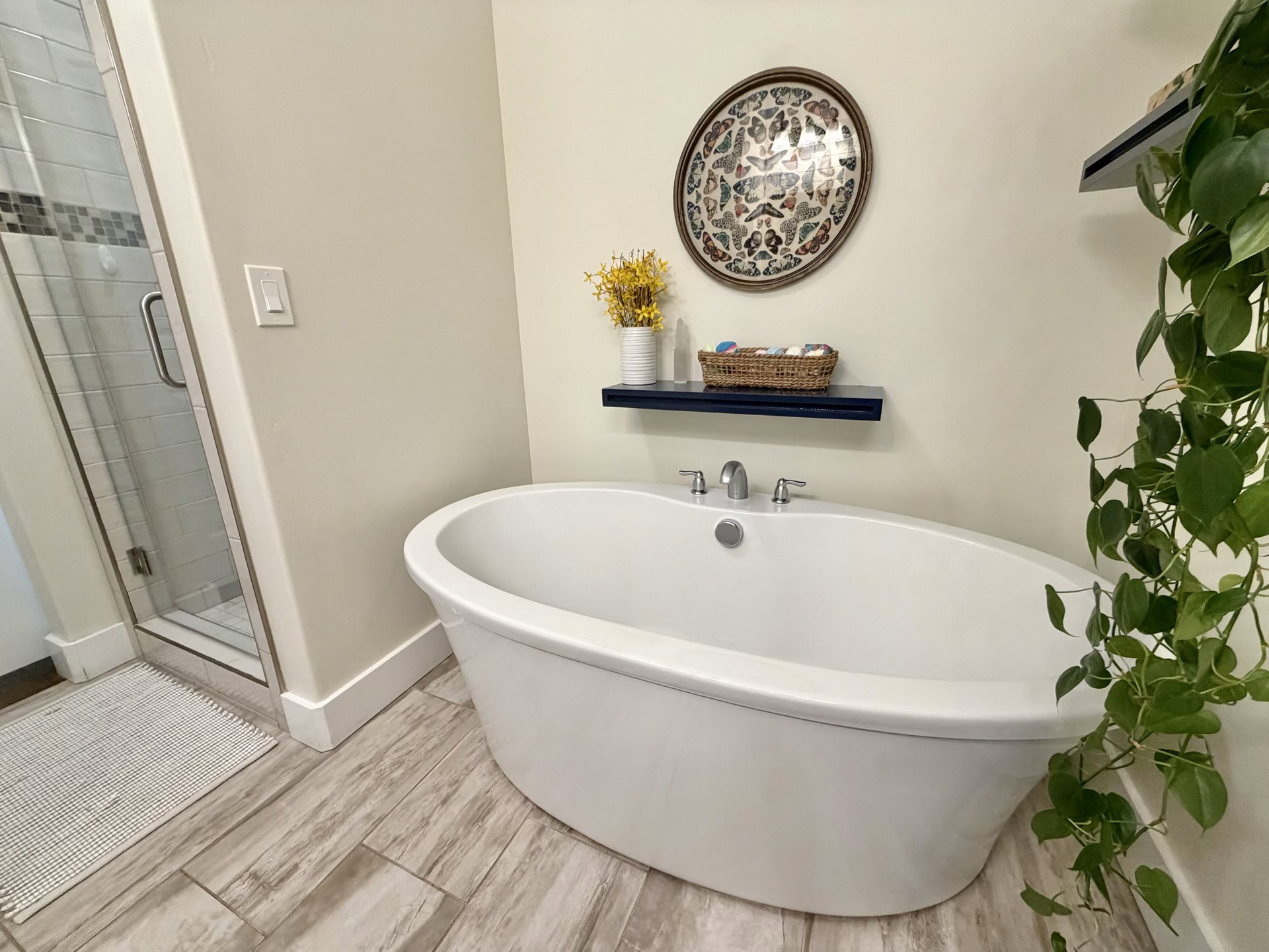 Freestanding soaking tub with chrome fixtures and wood-finish tile flooring